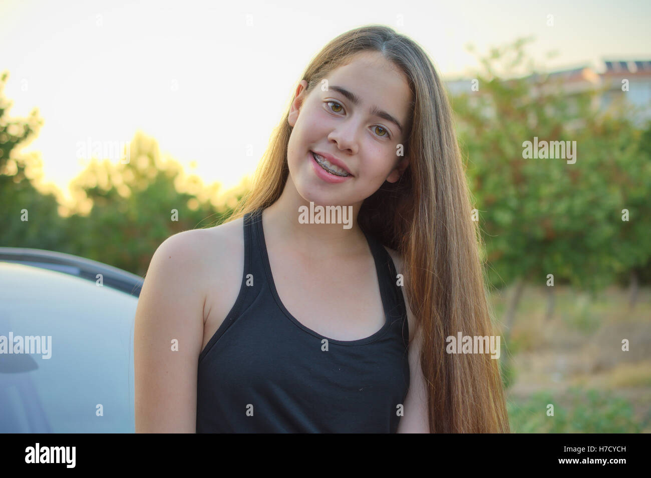 A 13 year old teenage girl with braces on her teeth sitting on a car  enjoying the Israeli summer sunset Stock Photo