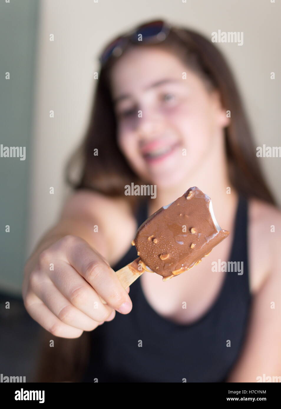 A 13 year old teenage girl celebrating the beginning of summer by eating a vanilla ice cream bar covered with chocolate and almo Stock Photo