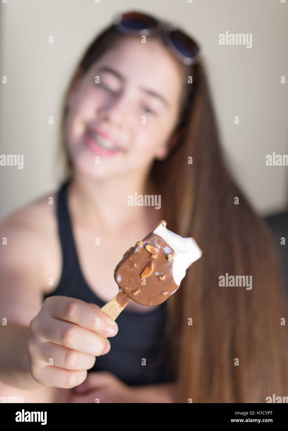 A 13 year old teenage girl celebrating the beginning of summer by eating a vanilla ice cream bar covered with chocolate and almo Stock Photo