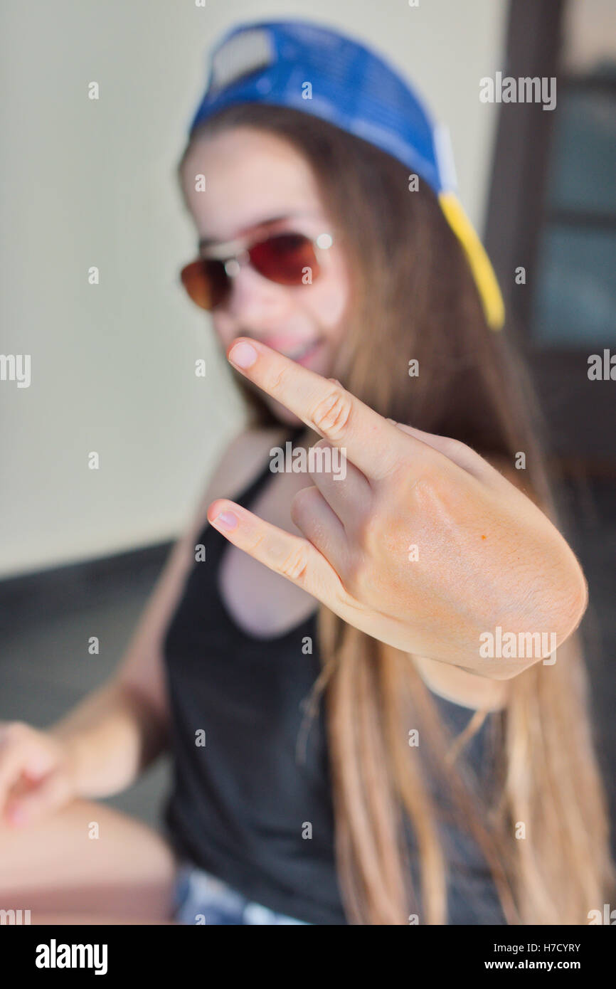 A cool 13 year old teenage girl in baseball cap and sunglasses making the Yo sign with her hand Stock Photo
