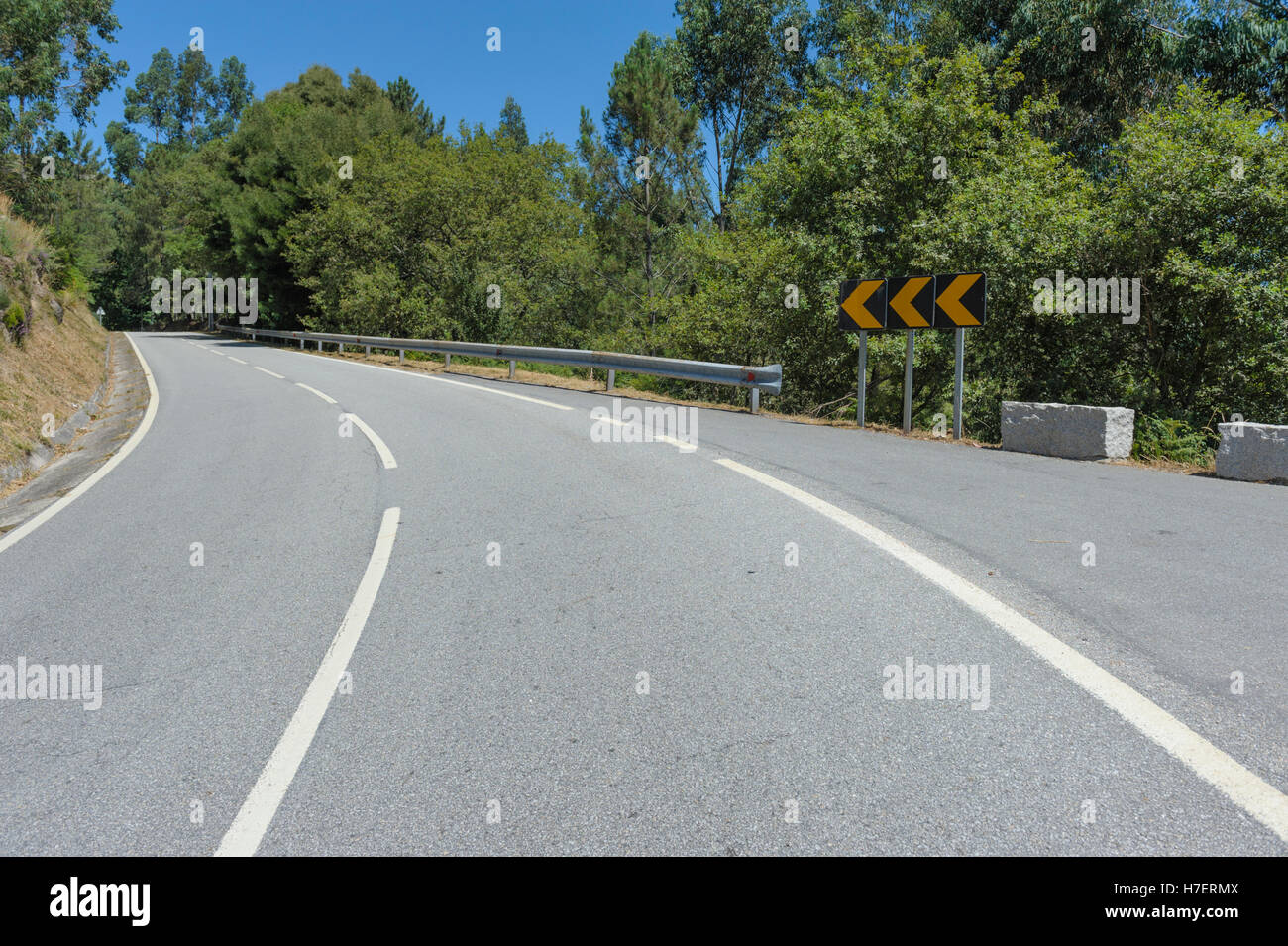 A bend in a rural road with signpost and white lines Stock Photo