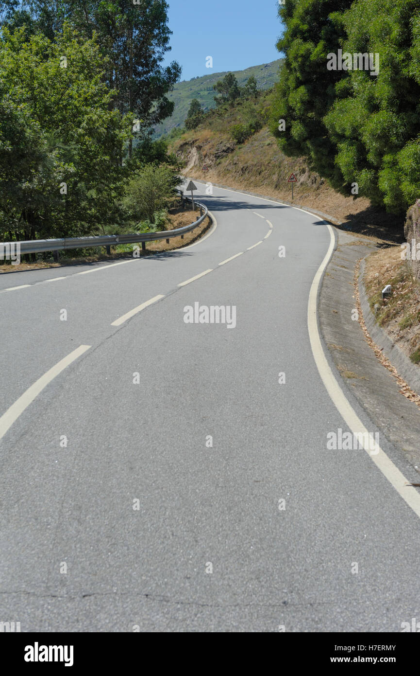 A bend in a rural road with signpost and white lines Stock Photo