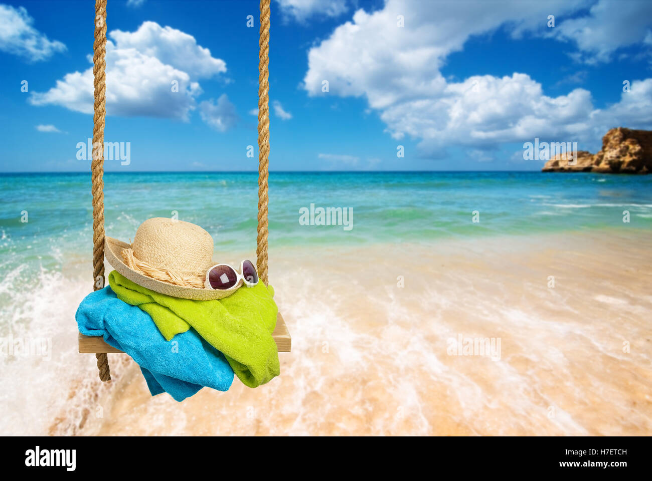 Summer rope swing with beach towels, sunhat and shades with beach blur ...