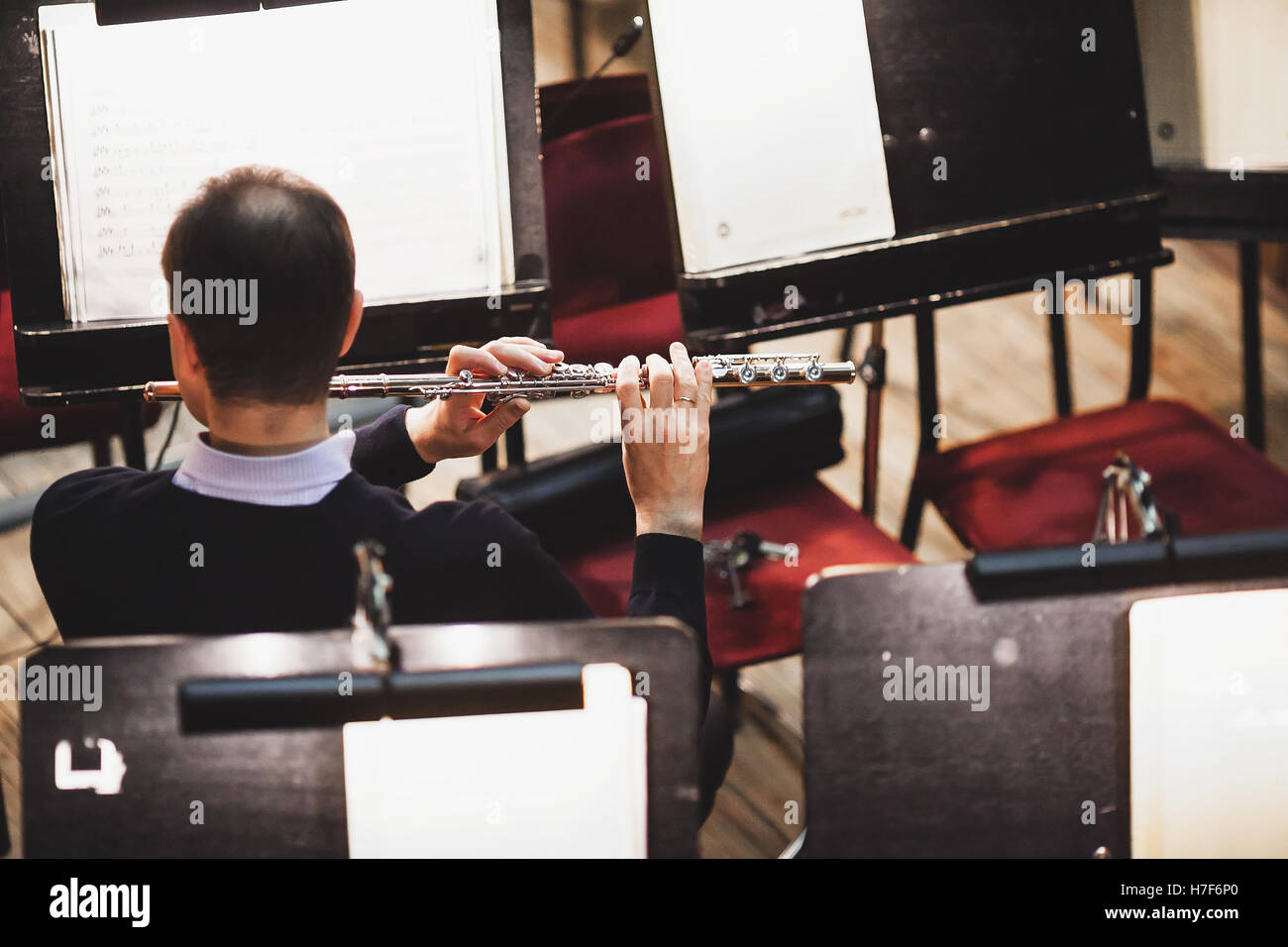 The man playing a flute in an orchestra pit. Sound orchestra close up
