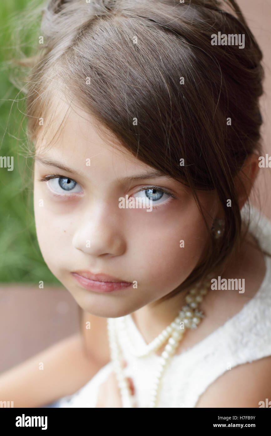 Young girl looking directly into the camera, wearing vintage pearl necklace and hair pulled back. Stock Photo