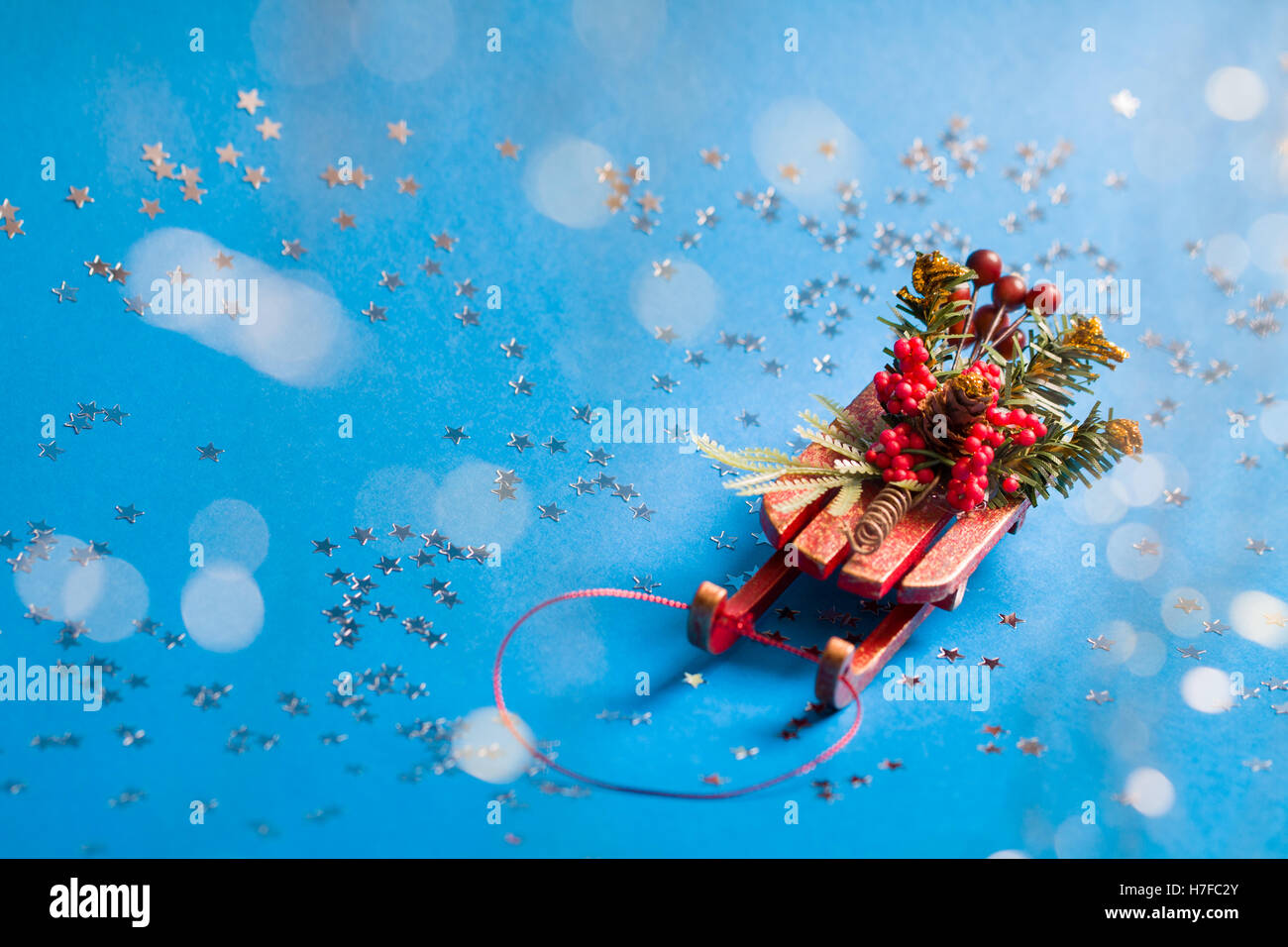 Christmas card with shine silver star and decorative sled standing on blue background in blurred glow balls. Stock Photo