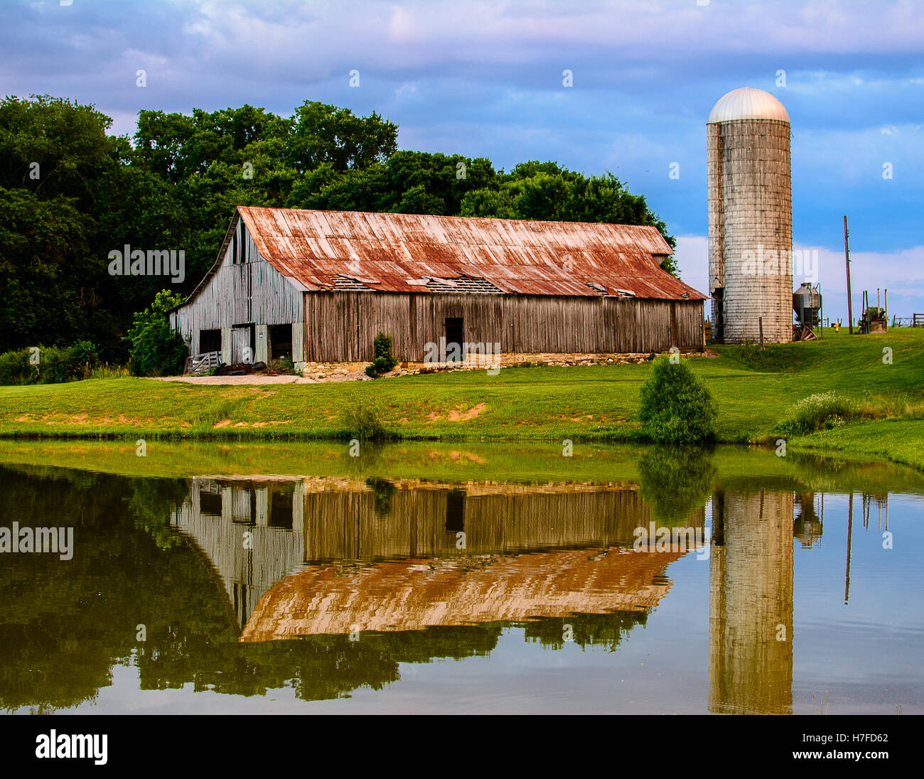 An old barn stands behind a lake carrying its reflection Stock Photo