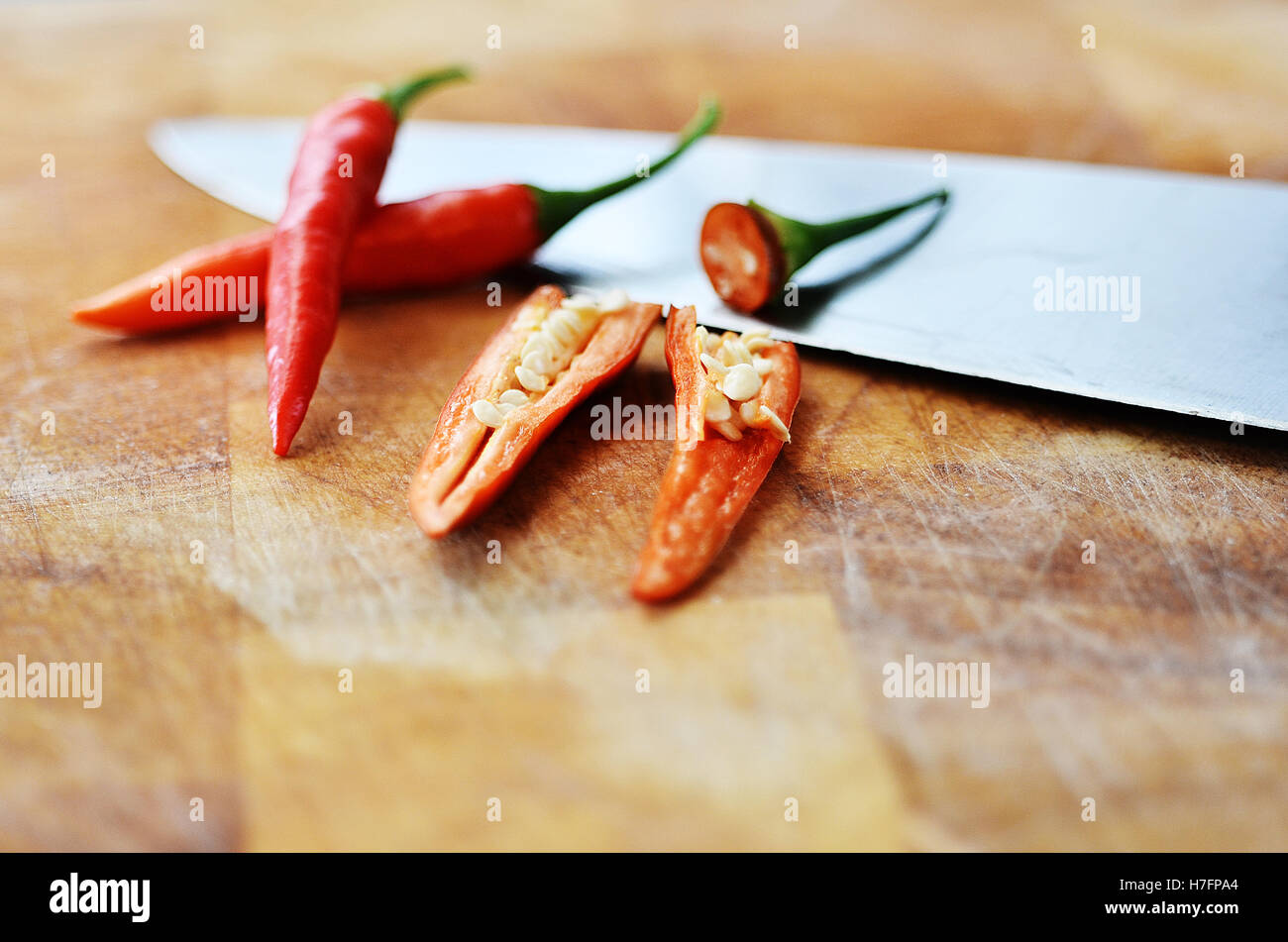 Sliced chilli peppers with seeds on a wooden chopping board with knife Stock Photo