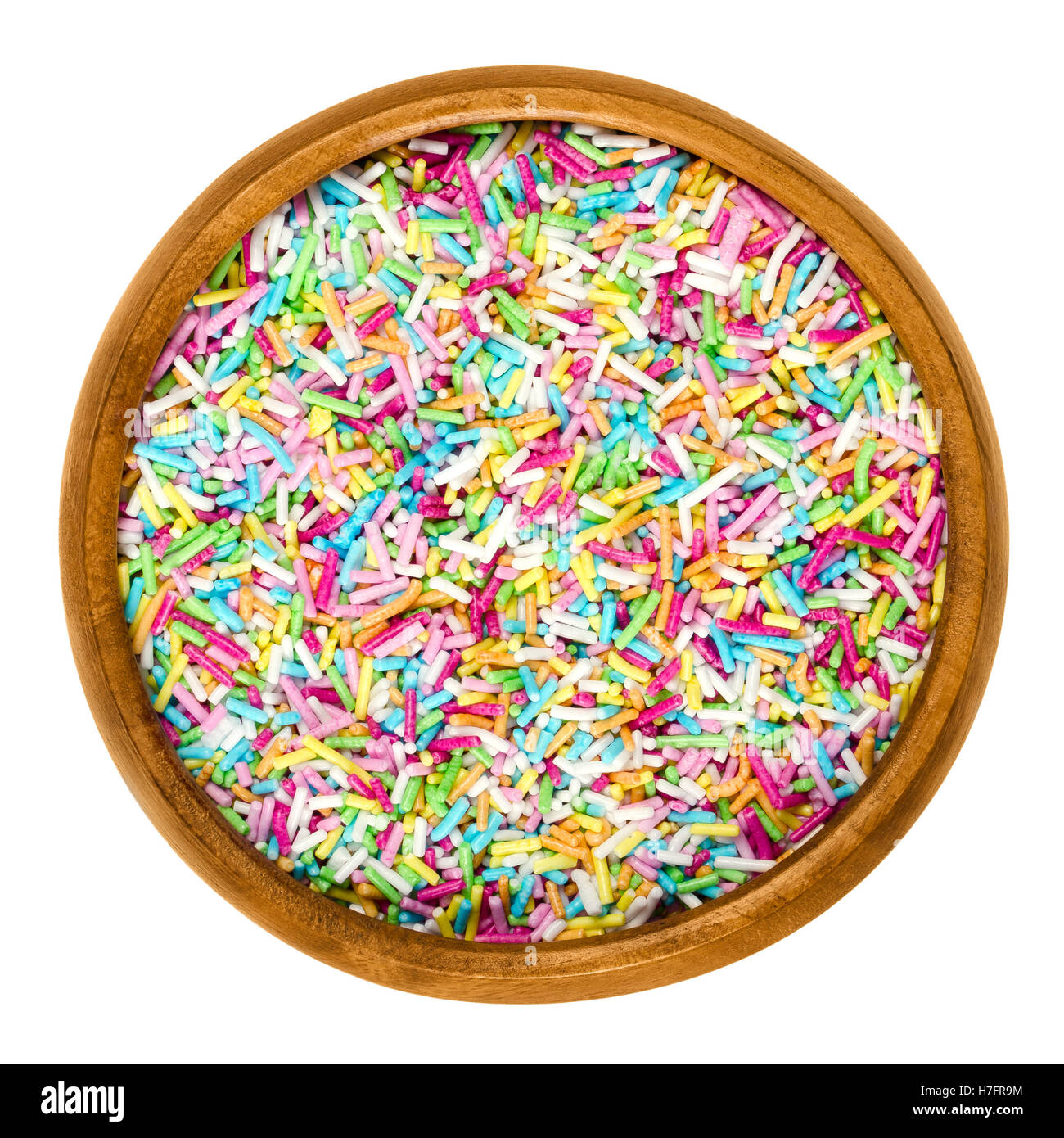 Colorful sugar sprinkles for food decorations in wooden bowl on white background. Multi colored bakery decoration ingredient. Stock Photo