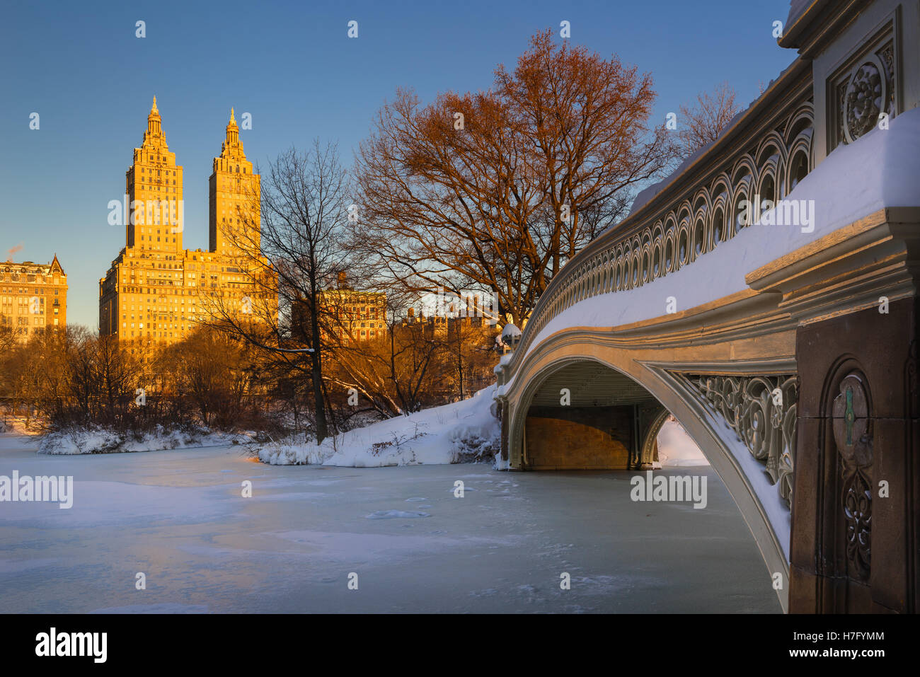 Central Park winter sunrise on the frozen Lake with the Bow Bridge and Upper West Side buildings. Manhattan, New York City Stock Photo