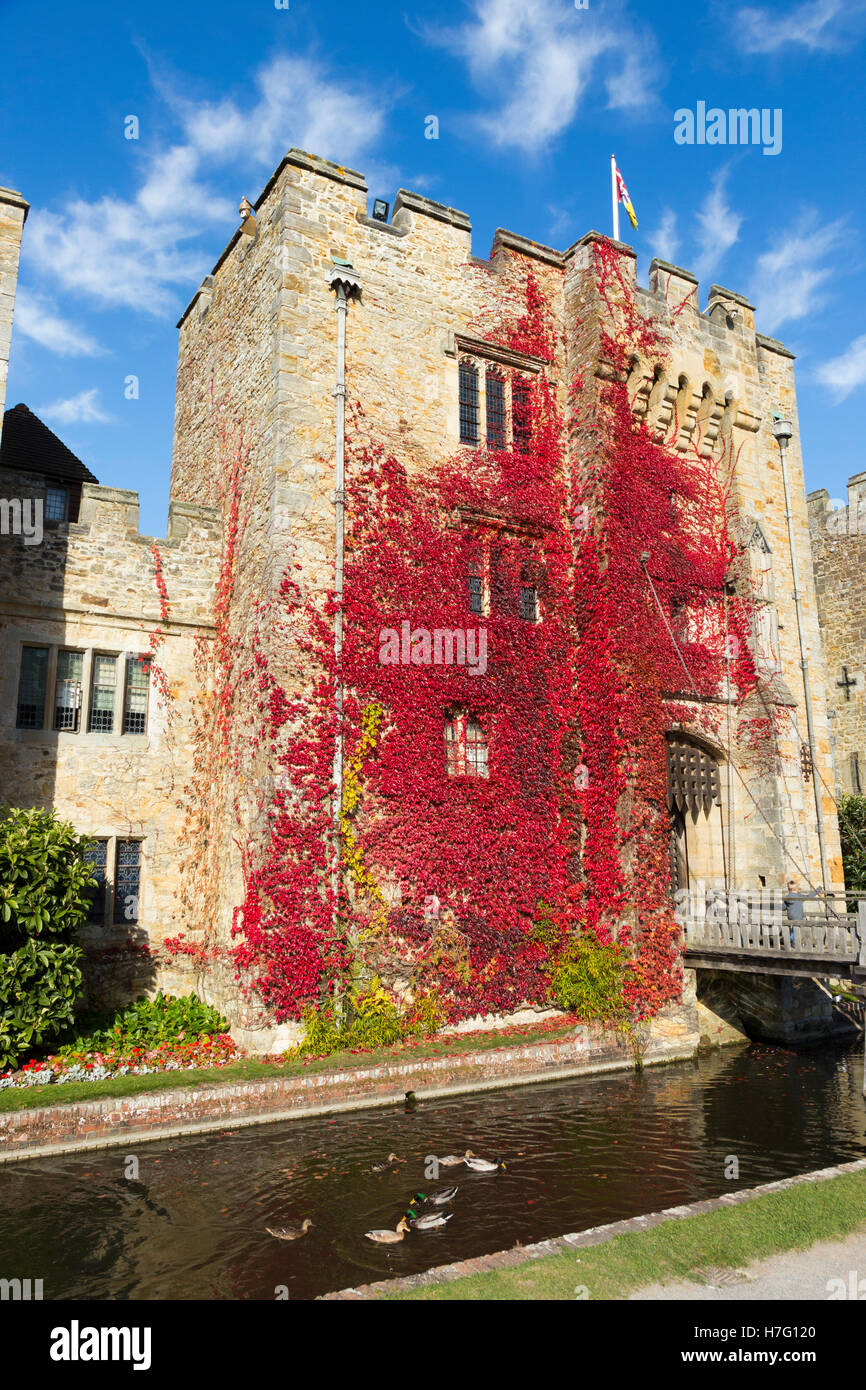 Hever Castle & moat, former home of Anne Boleyn, clad with red autumnal virginia creeper & blue sky / sunny skies / sun. Kent UK Stock Photo