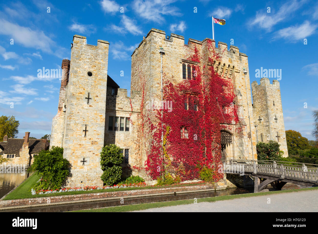 Hever Castle clad with red autumnal virginia creeper: Blue sky / sunny skies / sun & drawbridge / draw bridge over moat. Kent UK Stock Photo