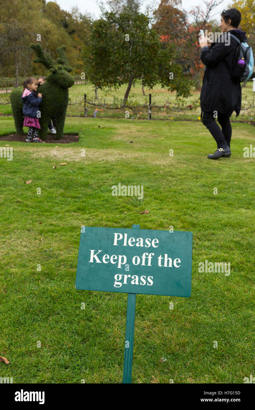 Please Keep off the grass / lawn sign, & people / tourists / tourist visitors / visitor ignoring the signs / breaking the rule. Stock Photo