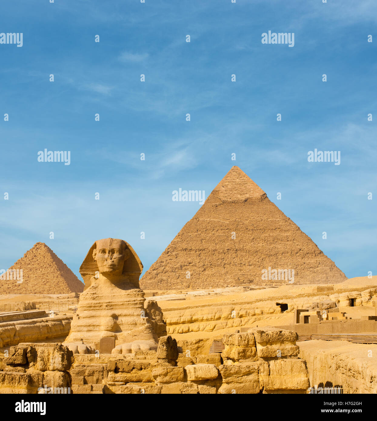 Front facing Sphinx and the large Egyptian Pyramids of Khafre, Menkaure slightly offset in front of blue sky in Cairo, Egypt Stock Photo