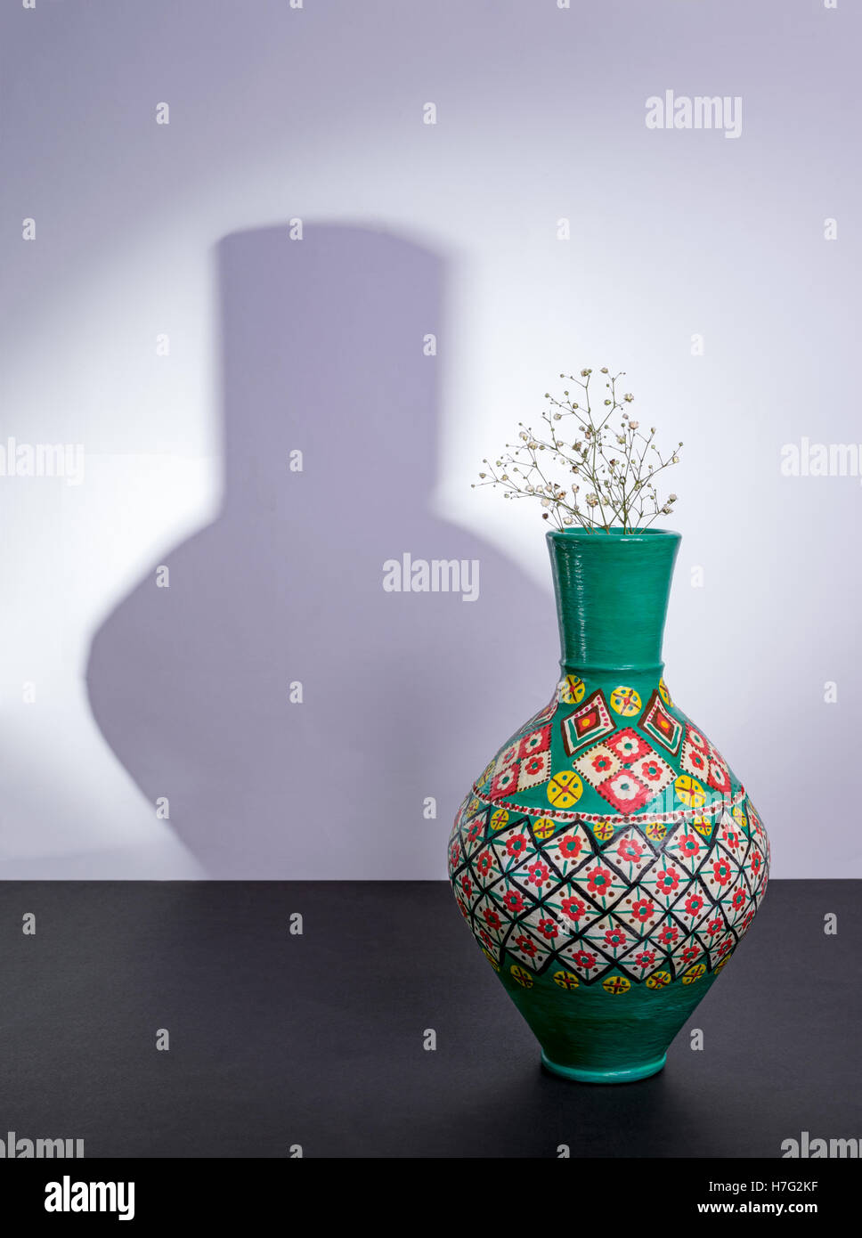 Colorful Egyptian traditional pottery vase, small white flowers with harsh shadow excluding