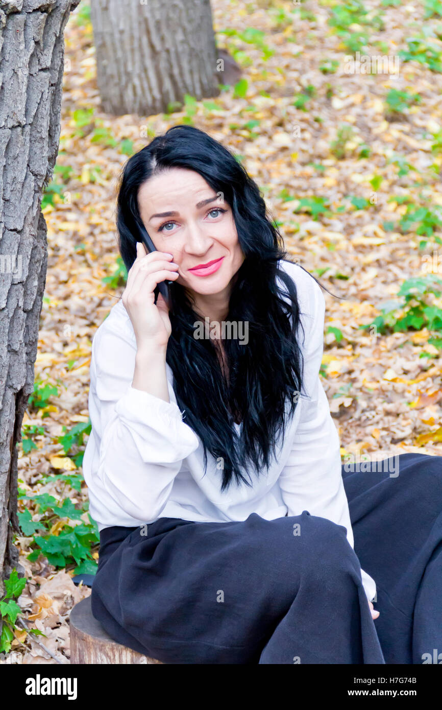 Caucasian brunette talking by cellular in autumn park Stock Photo