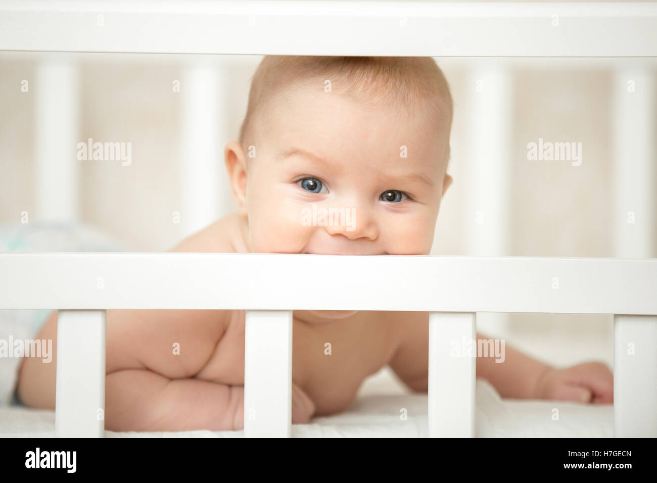 Cute child looking interested through the frame of baby crib Stock Photo