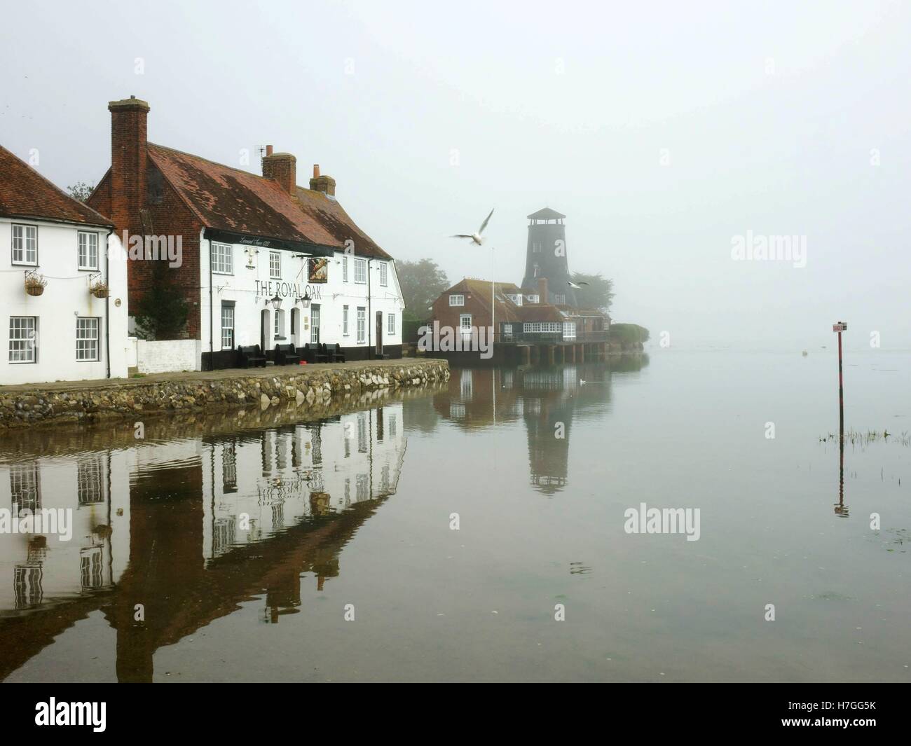 The Royal Oak traditional English pub and mill on a misty morning with reflections. Langstone Harbour, Havant, Hampshire, UK Stock Photo