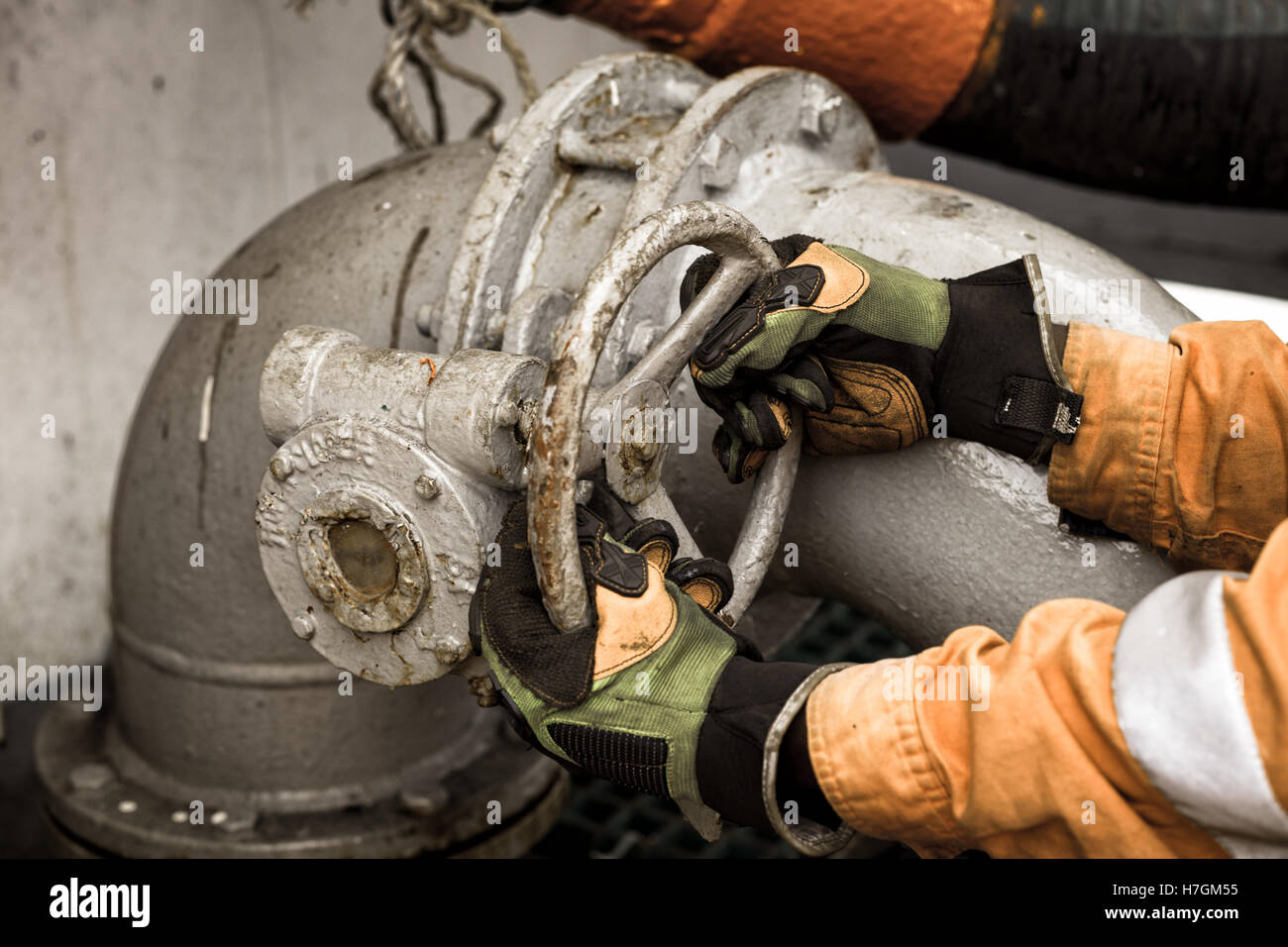 Man in safety gloves and orange coverall is opening/closing pipe valve Stock Photo