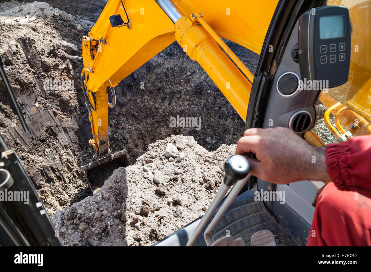 An excavator digging a hole in the ground seen from the cabin. Stock Photo