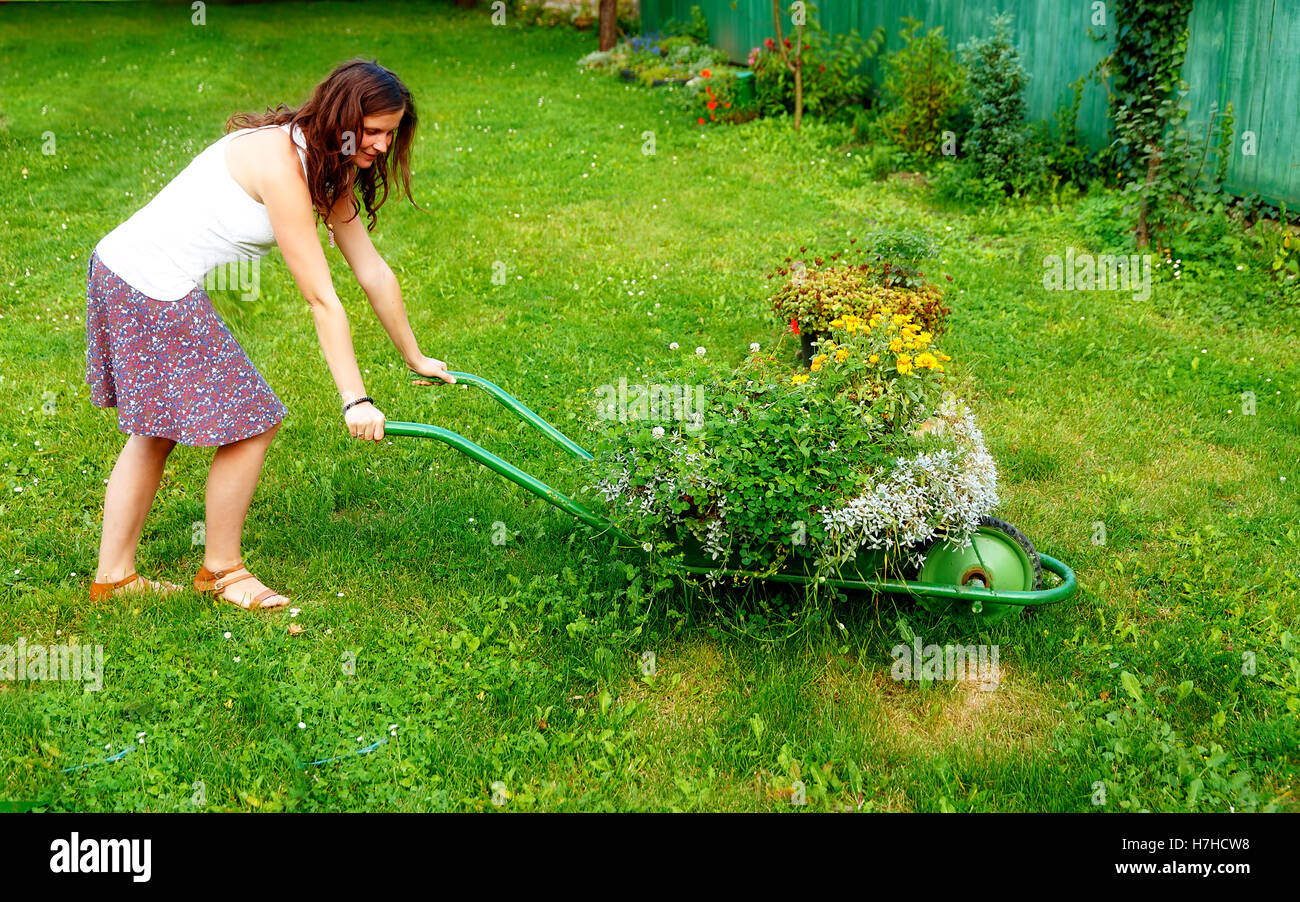 young woman in garden playfully pushing decorative wheelbarrow full of ...