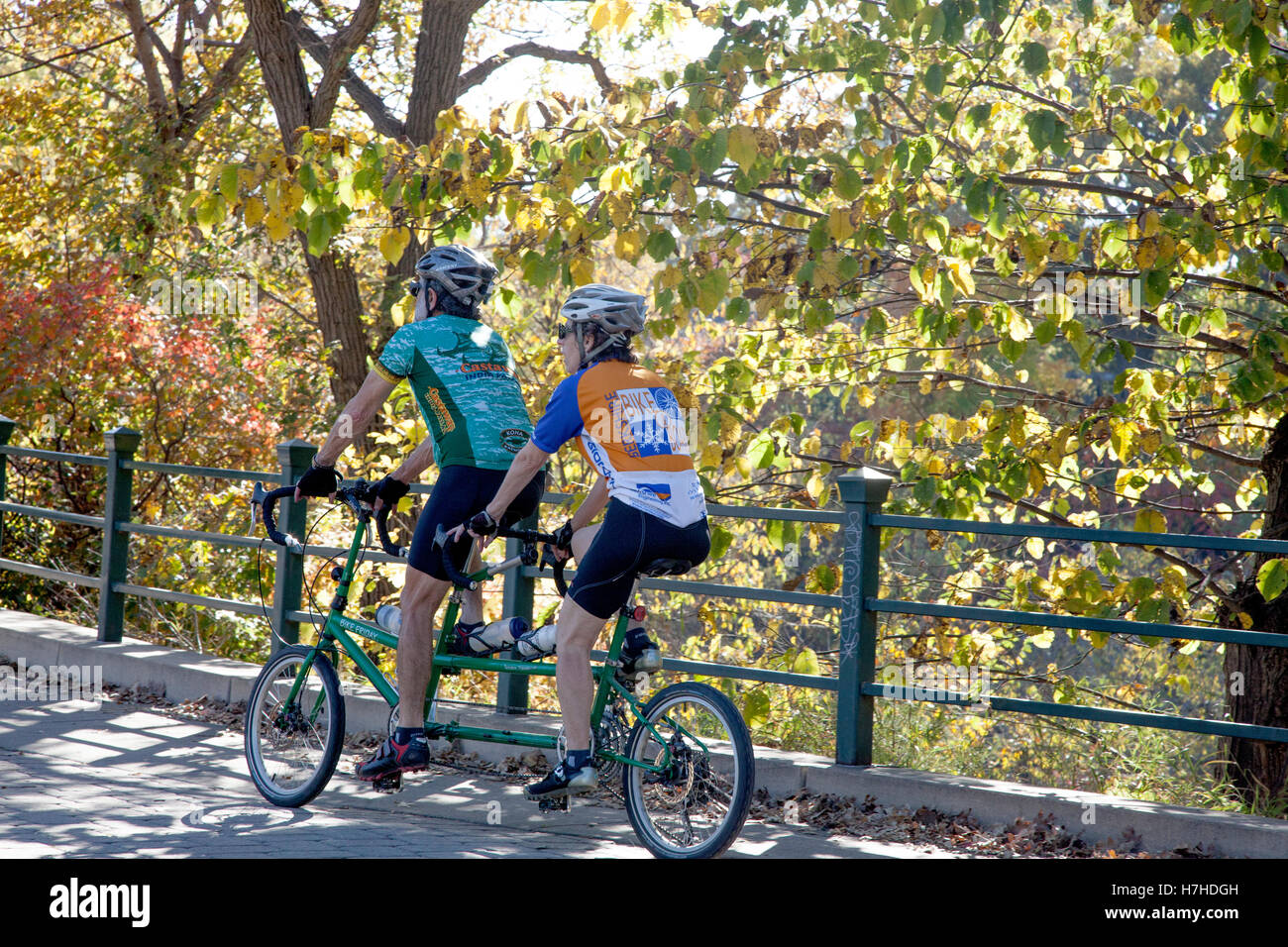 Helmeted man and woman riding a small wheeled tandem bicycle through Minnehaha park. Minneapolis Minnesota MN USA Stock Photo