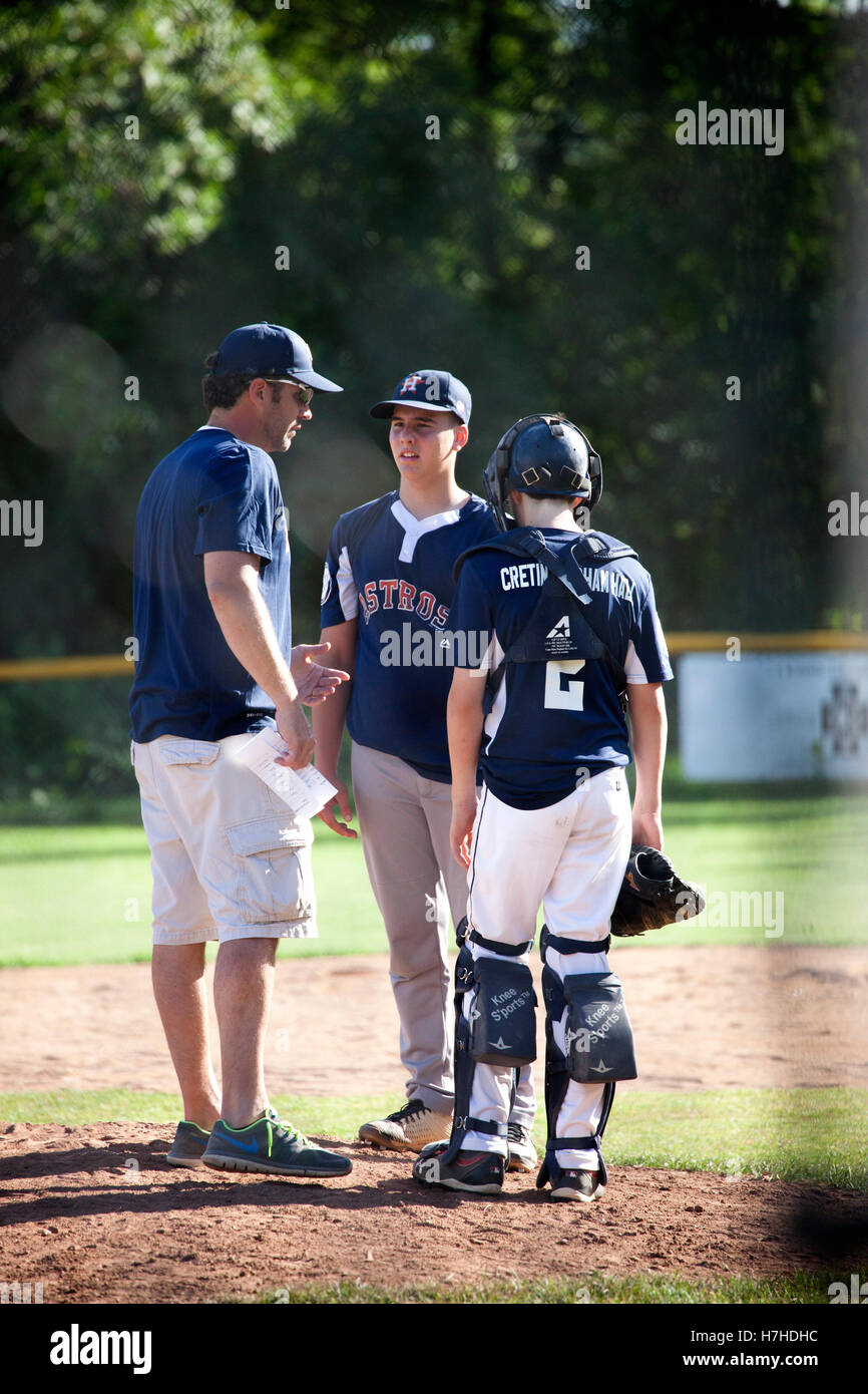 Baseball coach talking to teenage pitcher and catcher at the mound about game strategy. St Paul Minnesota MN USA Stock Photo