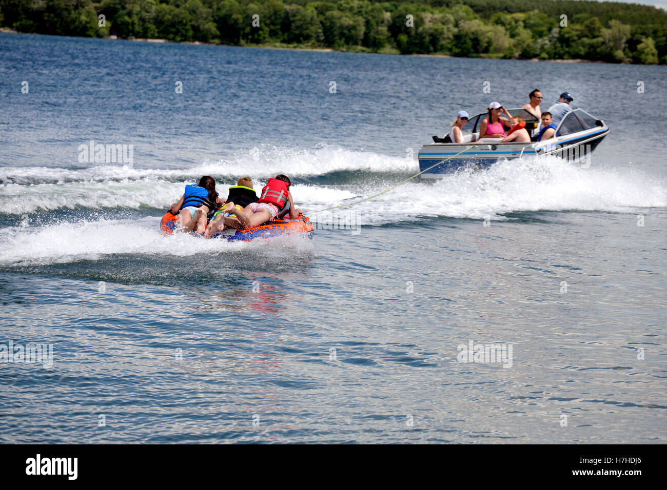 Parents pull three kids on a water tube with a speed boat on a lake. Clitherall Minnesota MN USA Stock Photo