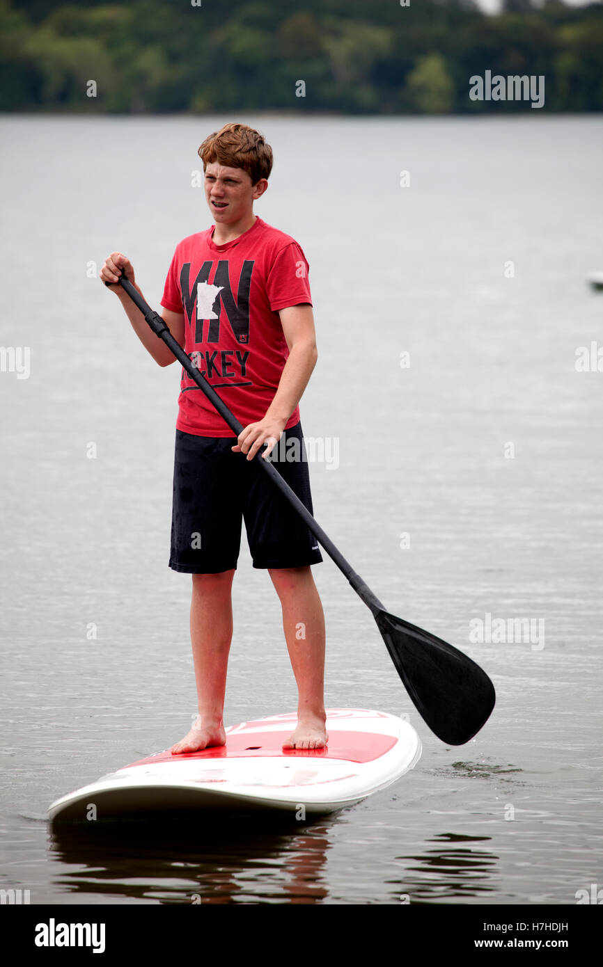 Teenage boy on a stand up paddle board paddling on a lake. Clitherall Minnesota MN USA Stock Photo