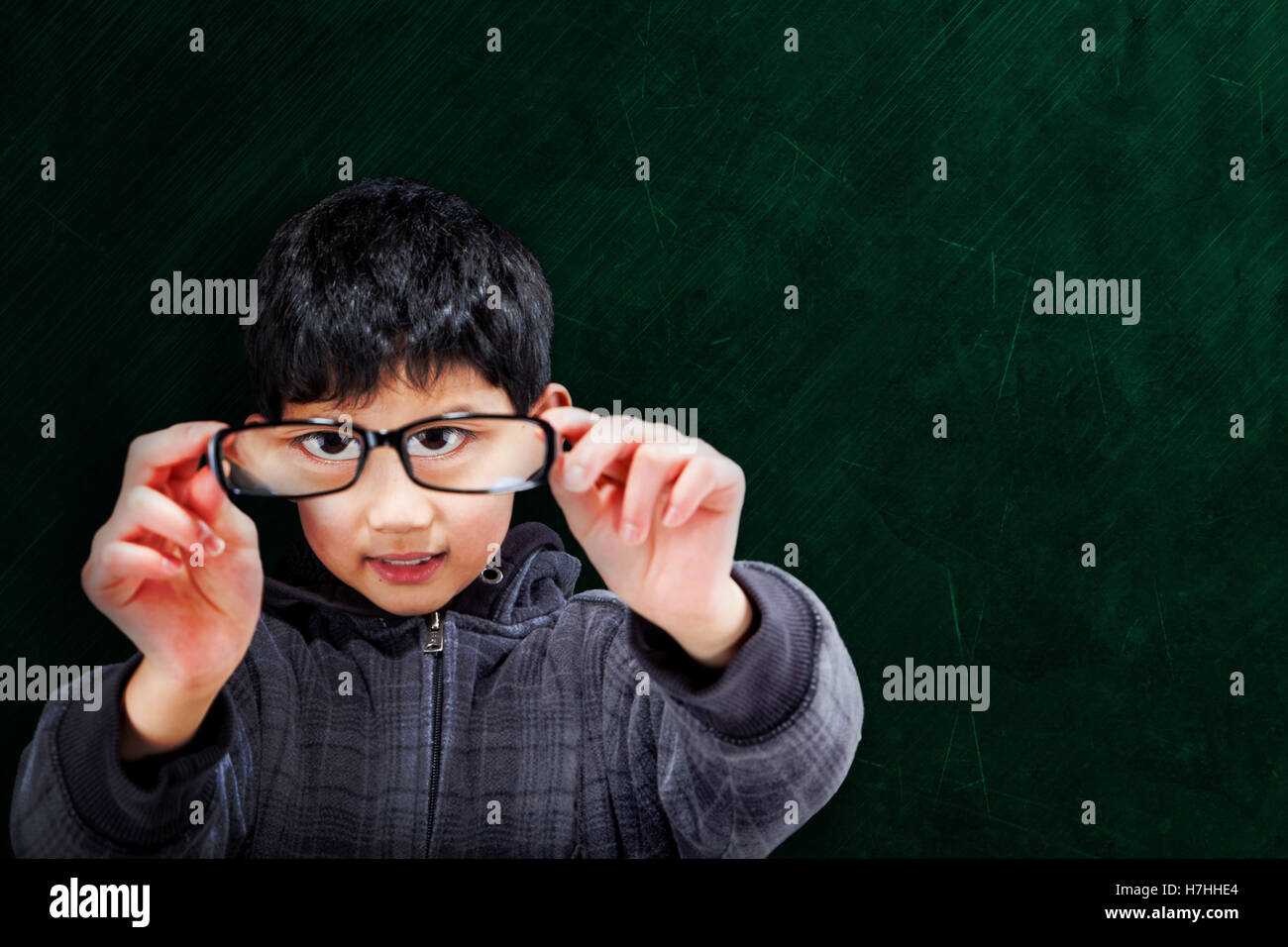 Cute Asian boy holding up eyeglasses on chalkboard background with copy space. Stock Photo