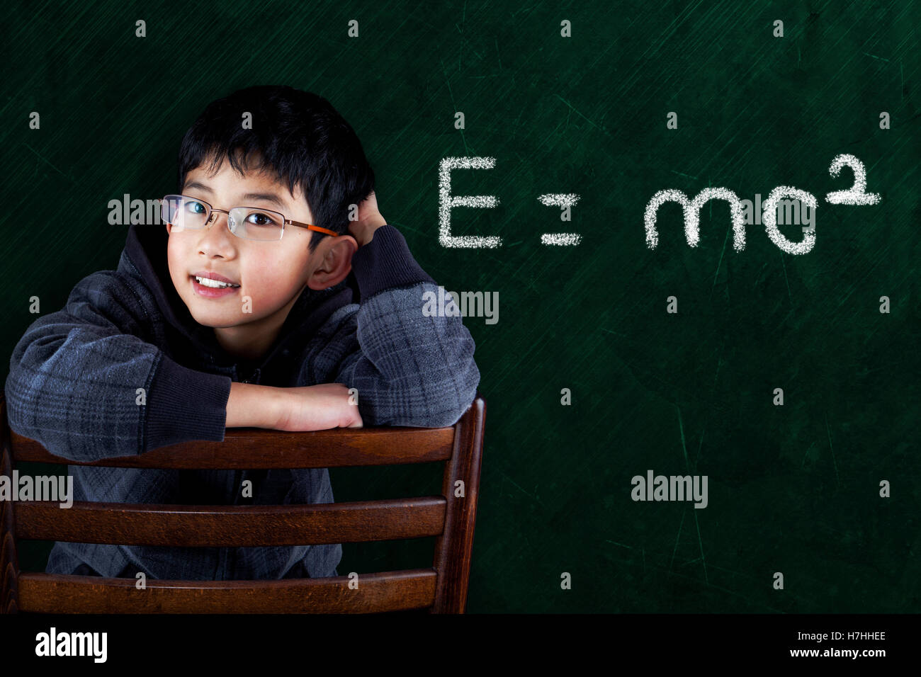 Smart Asian boy sitting on classroom chair with Math equation on chalkboard background and copy space. Stock Photo