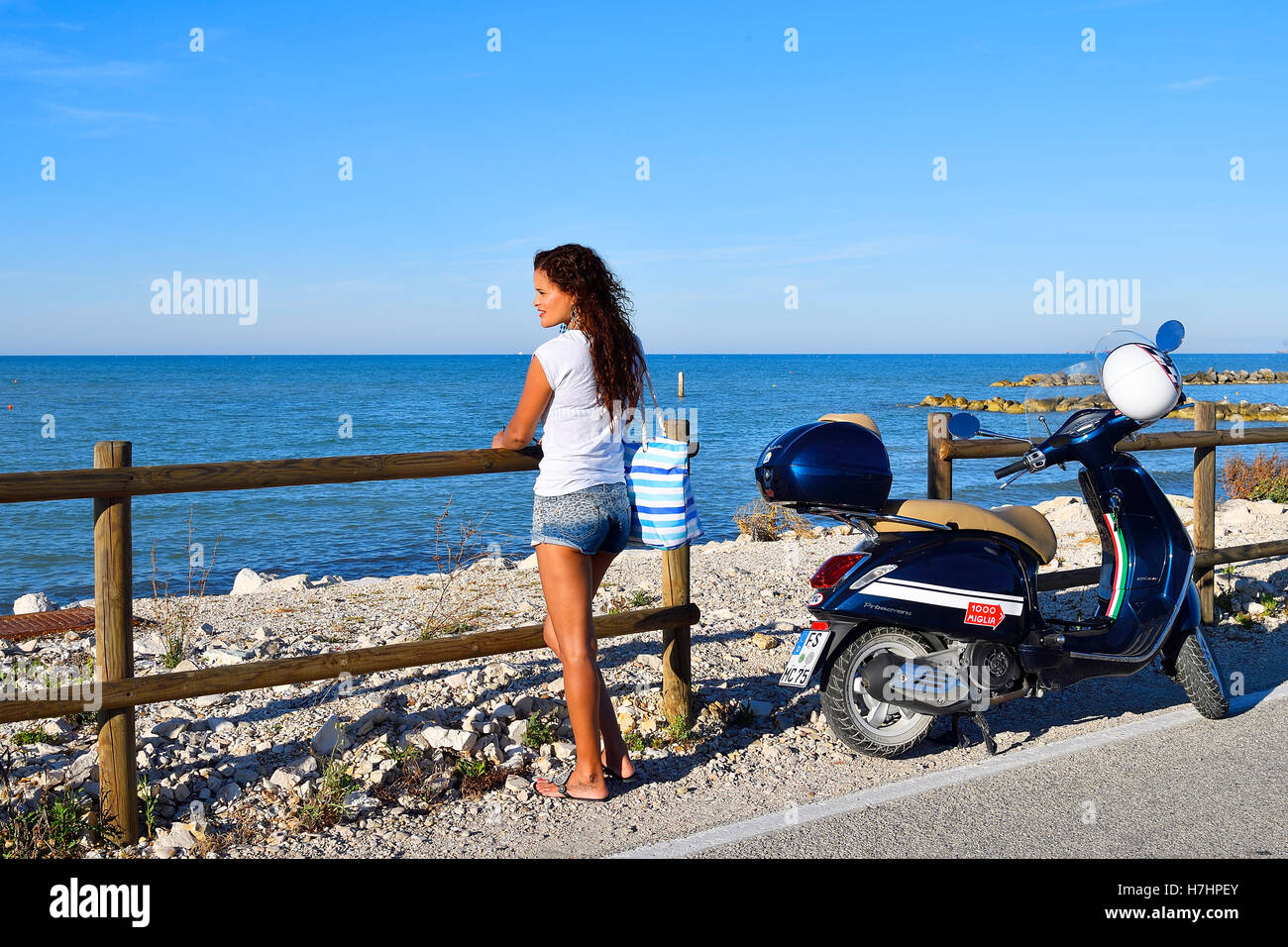 Woman gazing out at the sea next to Vespa Primavera scooter, Marina di Montemarciano, Indian, Alaska Marche, Italy Stock Photo