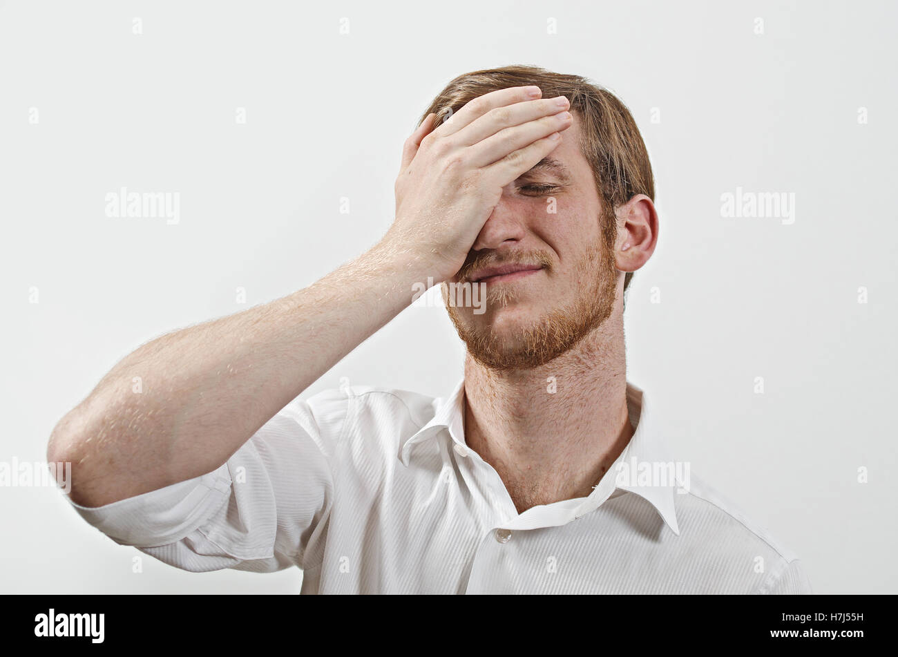 Young Adult Male Wearing White Shirt  Covers His Face by Hand, Gesturing He Has Made a Big Mistake Stock Photo