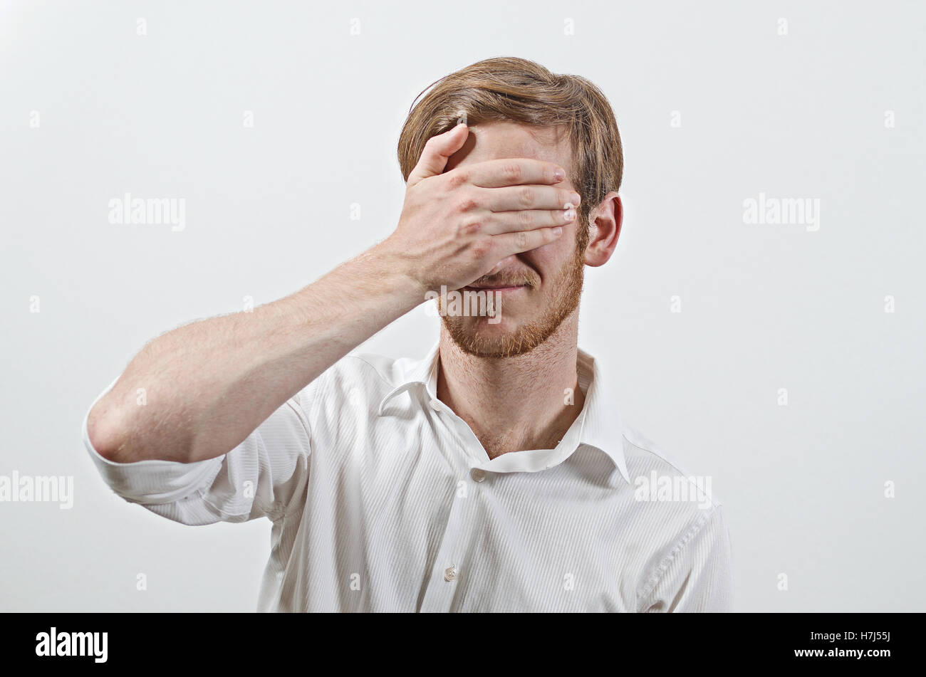 Young Adult Male Wearing White Shirt Covers His Face by Hand, Gesturing He Has Made a Big Mistake Stock Photo