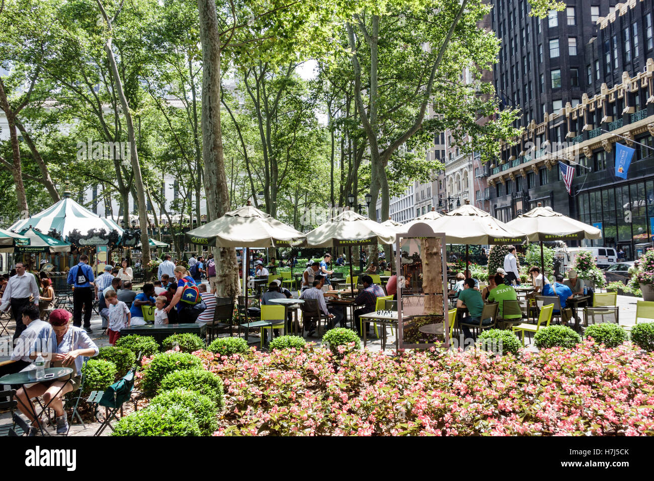 New York City,NY NYC Manhattan,Midtown,Bryant Park,public park,tabletop games,seating,umbrellas,flower bed,trees,adult,adults,man men male,woman femal Stock Photo
