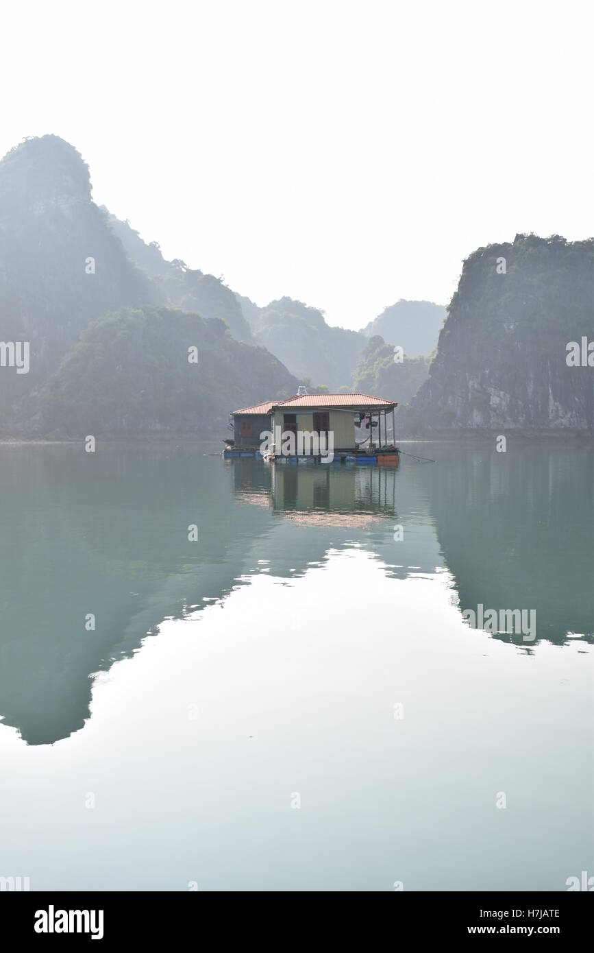Floating house with mountains reflecting in the water in Halong bay, Vietnam Stock Photo
