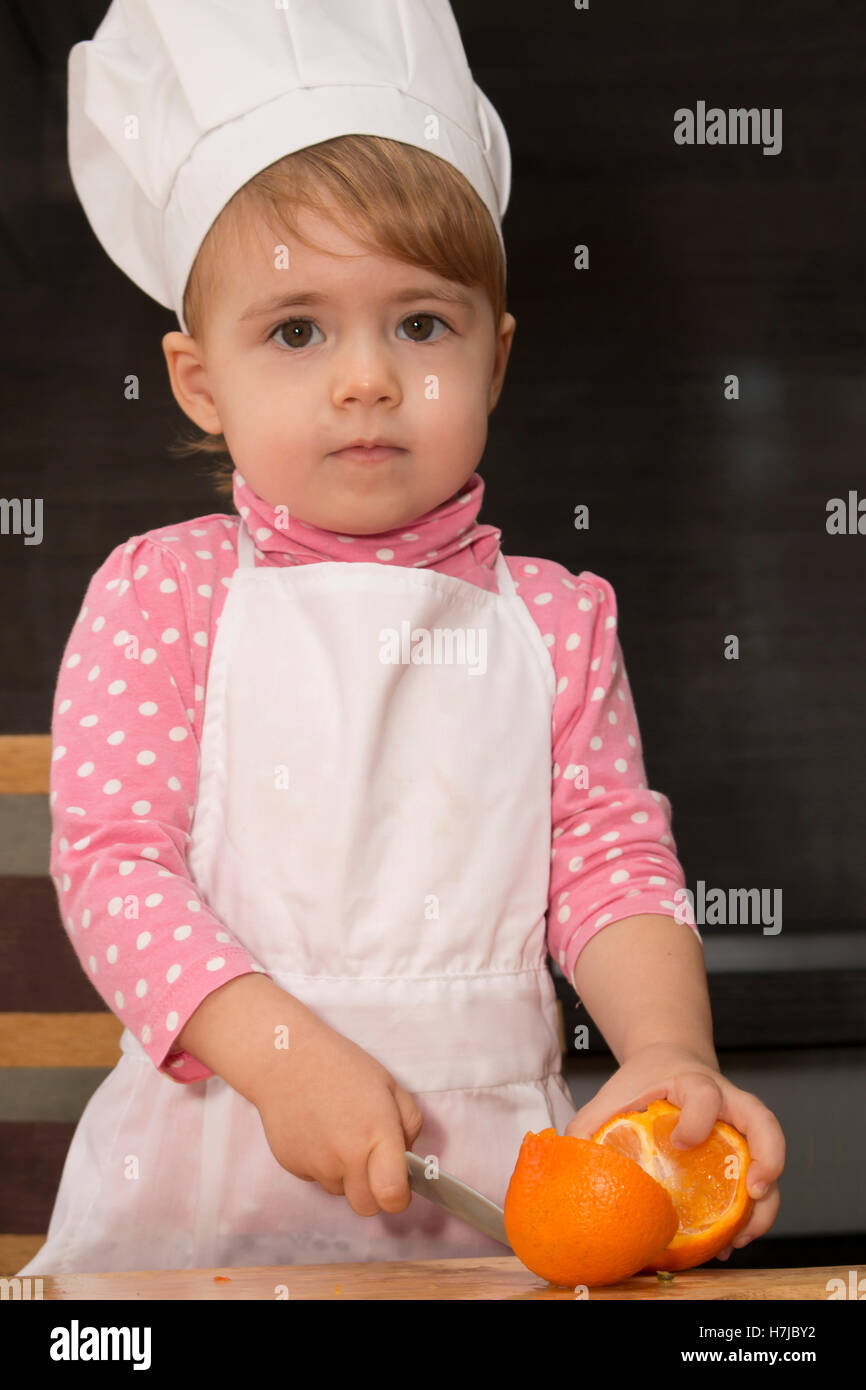 Little Cute Kid In A Cook Cap On Kitchen Cuts Oranges Mother S