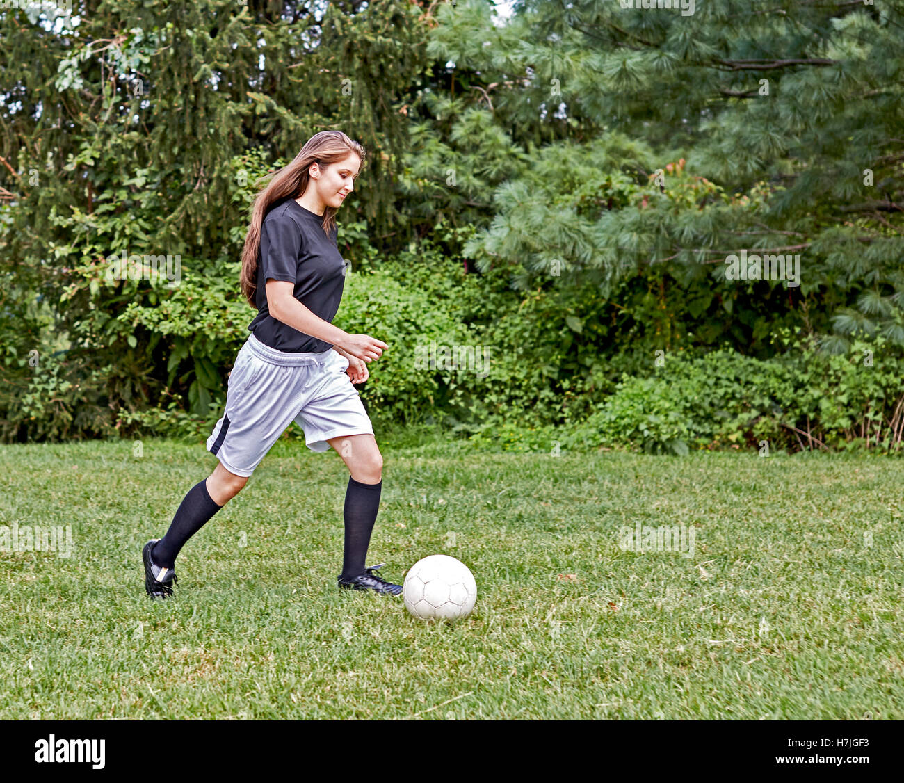 Young girl on the grass kicking a soccer ball and smiling Stock Photo