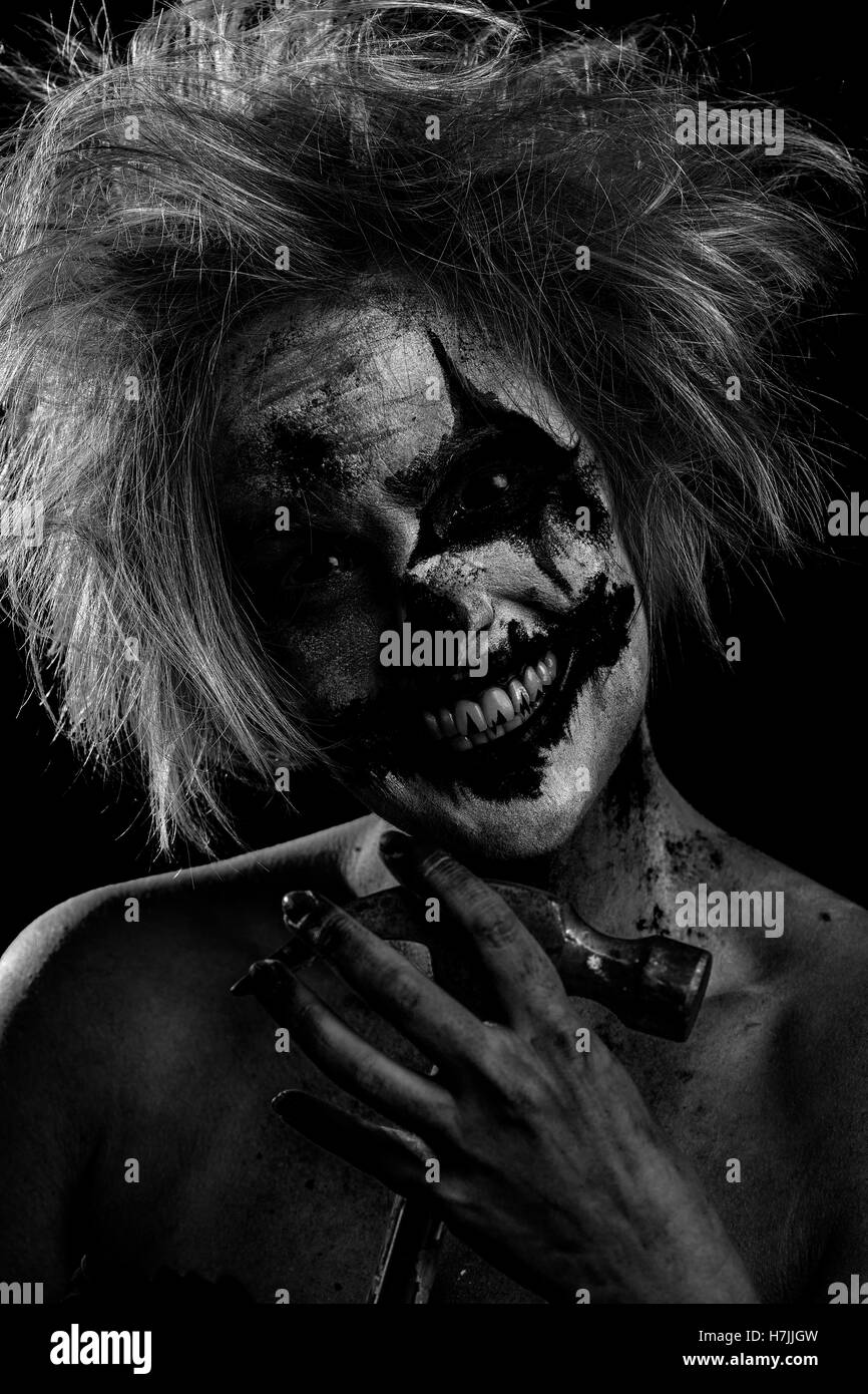 Blonde female model as bloodstained, crazed, insane, murderous clown with hammer, black and white Stock Photo