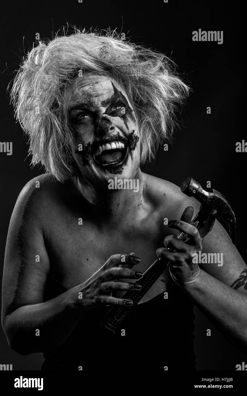 Blonde female model as bloodstained, crazed insane murderous clown with hammer, black and white Stock Photo