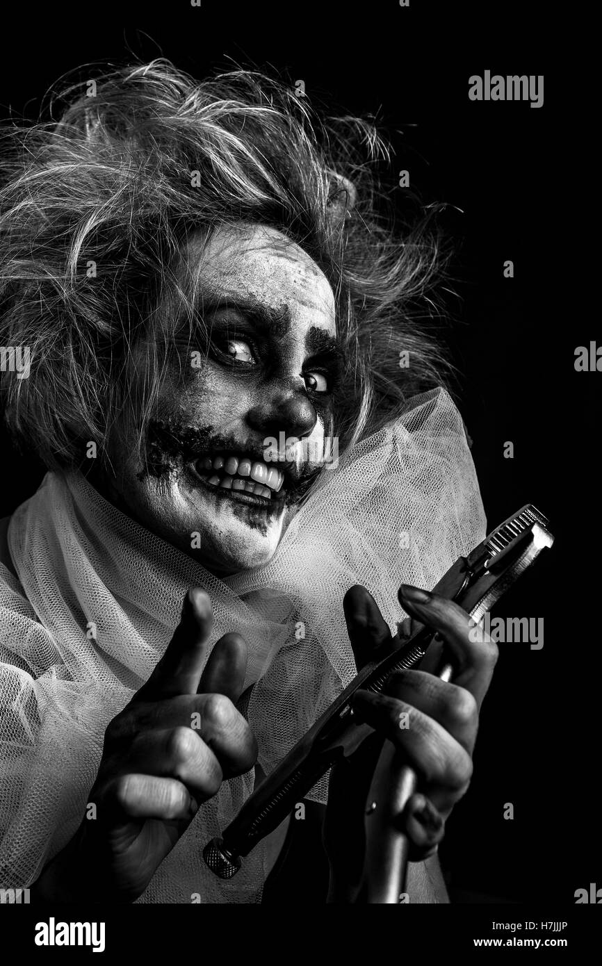 Blonde female model as crazed, insane, murderous clown pointing at you, holding wrench Stock Photo