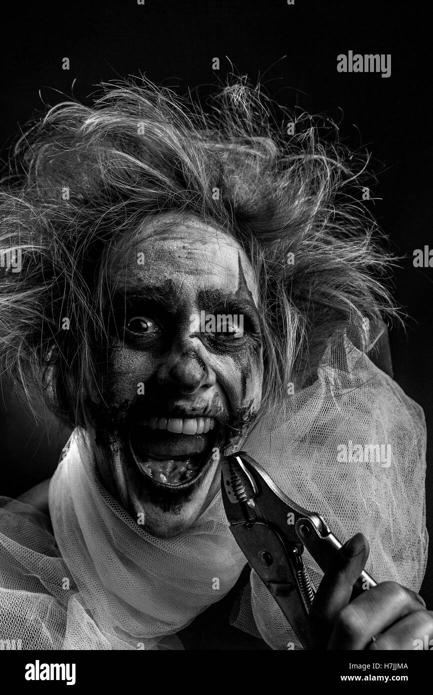 Blonde female model as twisted insane bloodstained clown with wrench Stock Photo