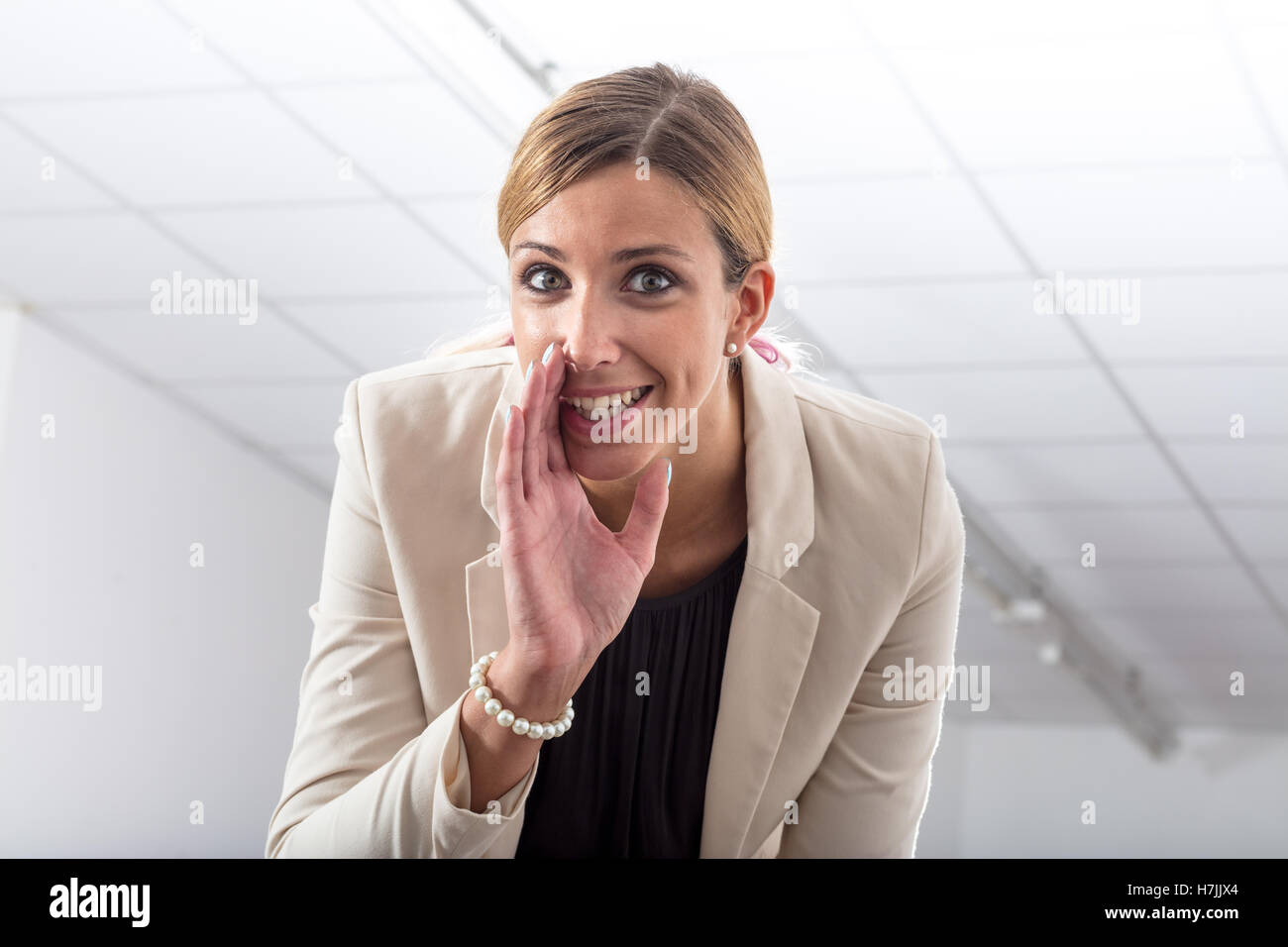 Office gossip whispering a secret as a stylish businesswoman leans down towards the camera with a gleeful expression to whisper Stock Photo