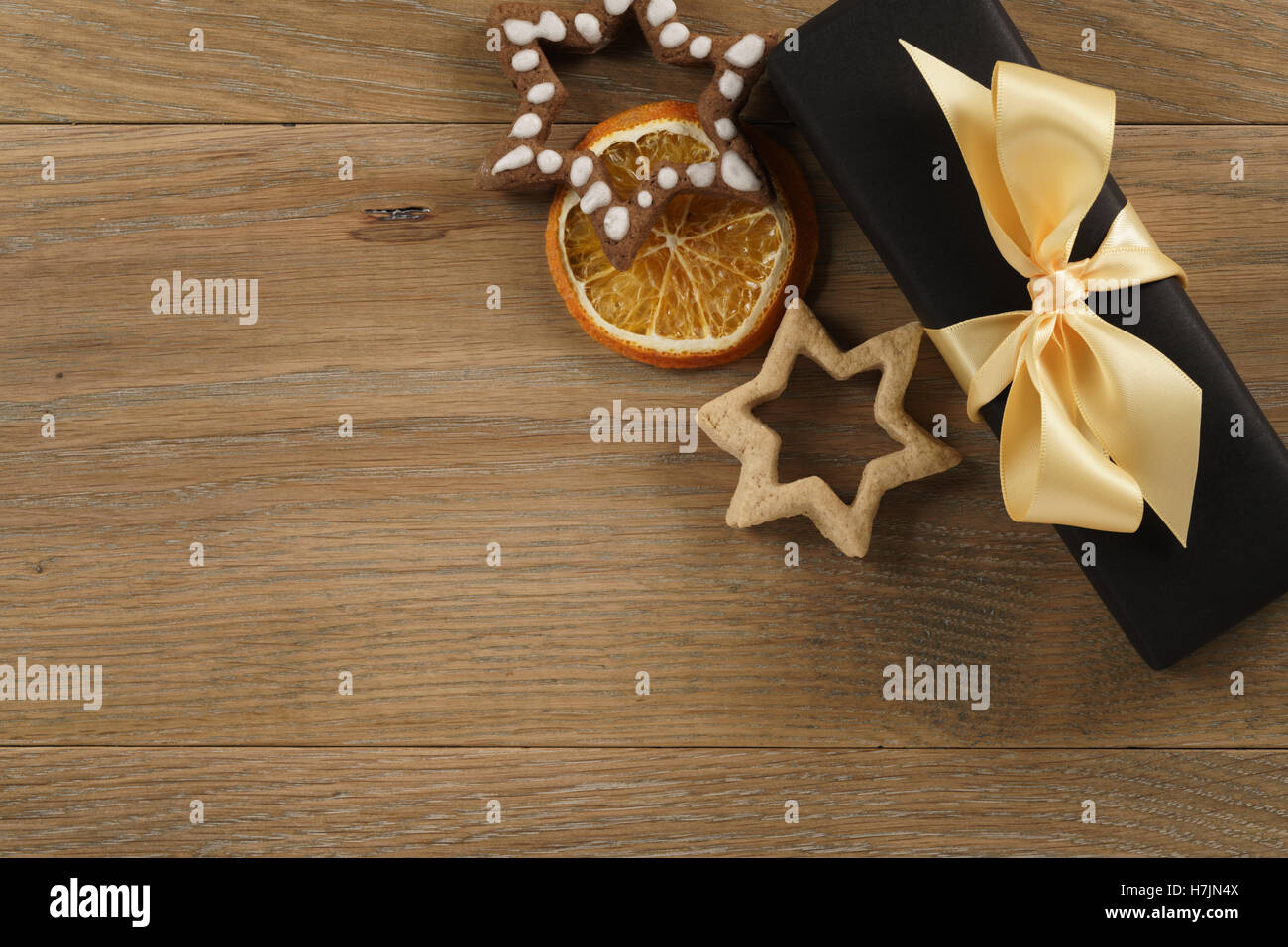 black gift box with golden ribbon bow and christmas cookies on wood table Stock Photo