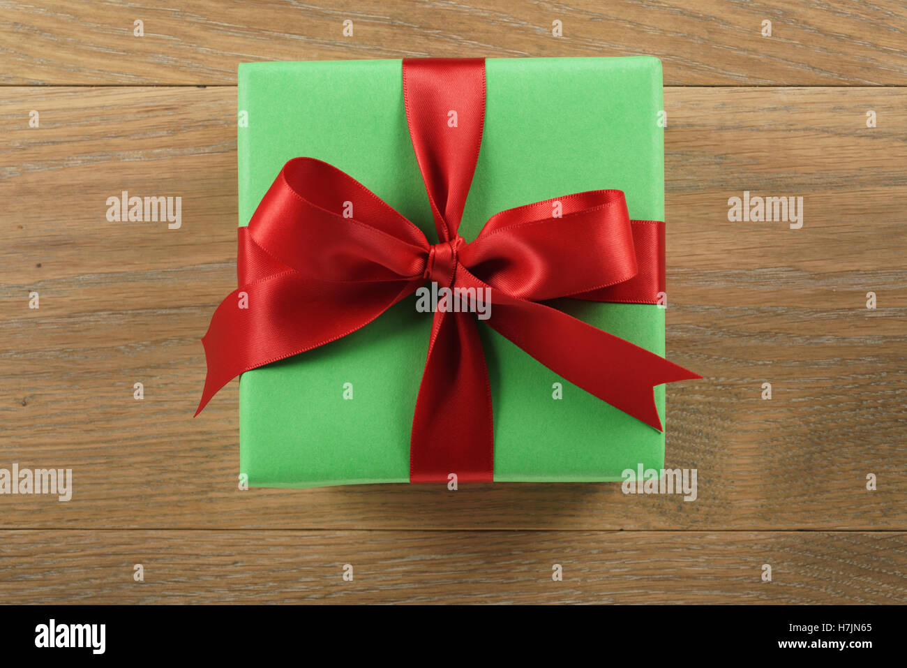 green gift box with red ribbon bow on wooden oak table from above Stock Photo