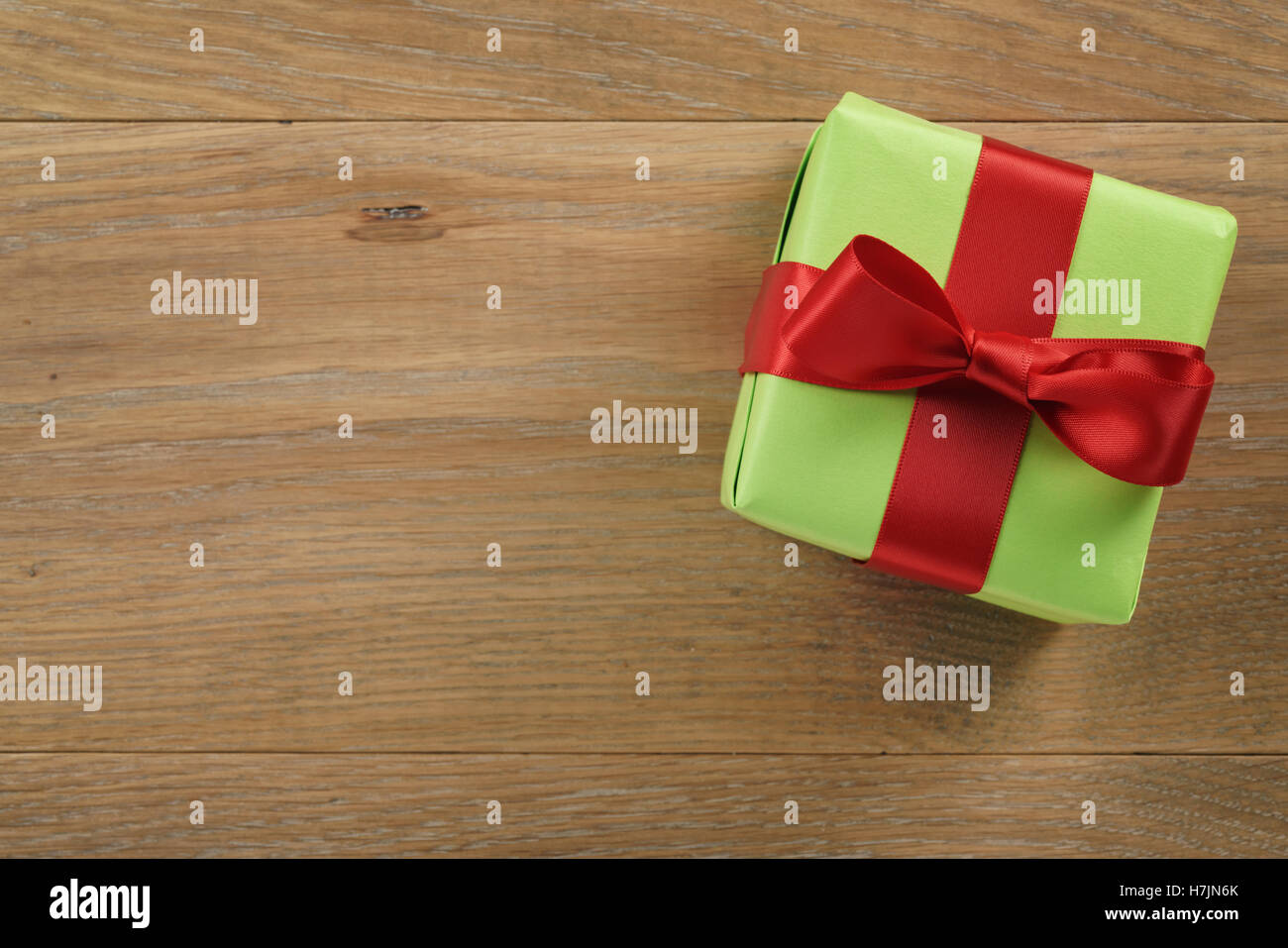 green gift box with red ribbon bow on wooden oak table from above Stock Photo