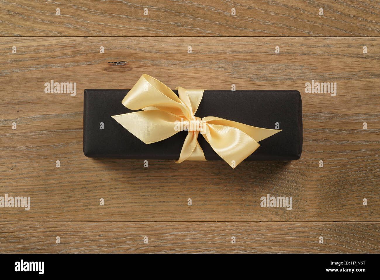 black rectangle gift box with champagne color ribbon bow on wooden oak table from above Stock Photo