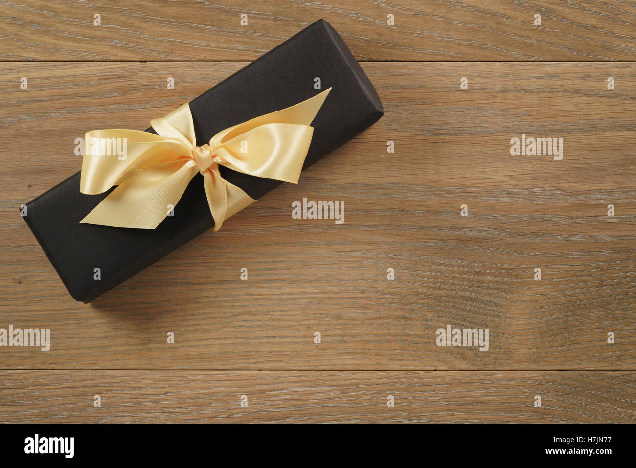 black rectangle gift box with champagne color ribbon bow on wooden oak table from above Stock Photo