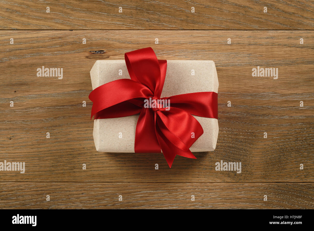 brown gift box with red ribbon bow on wooden oak table from above Stock Photo