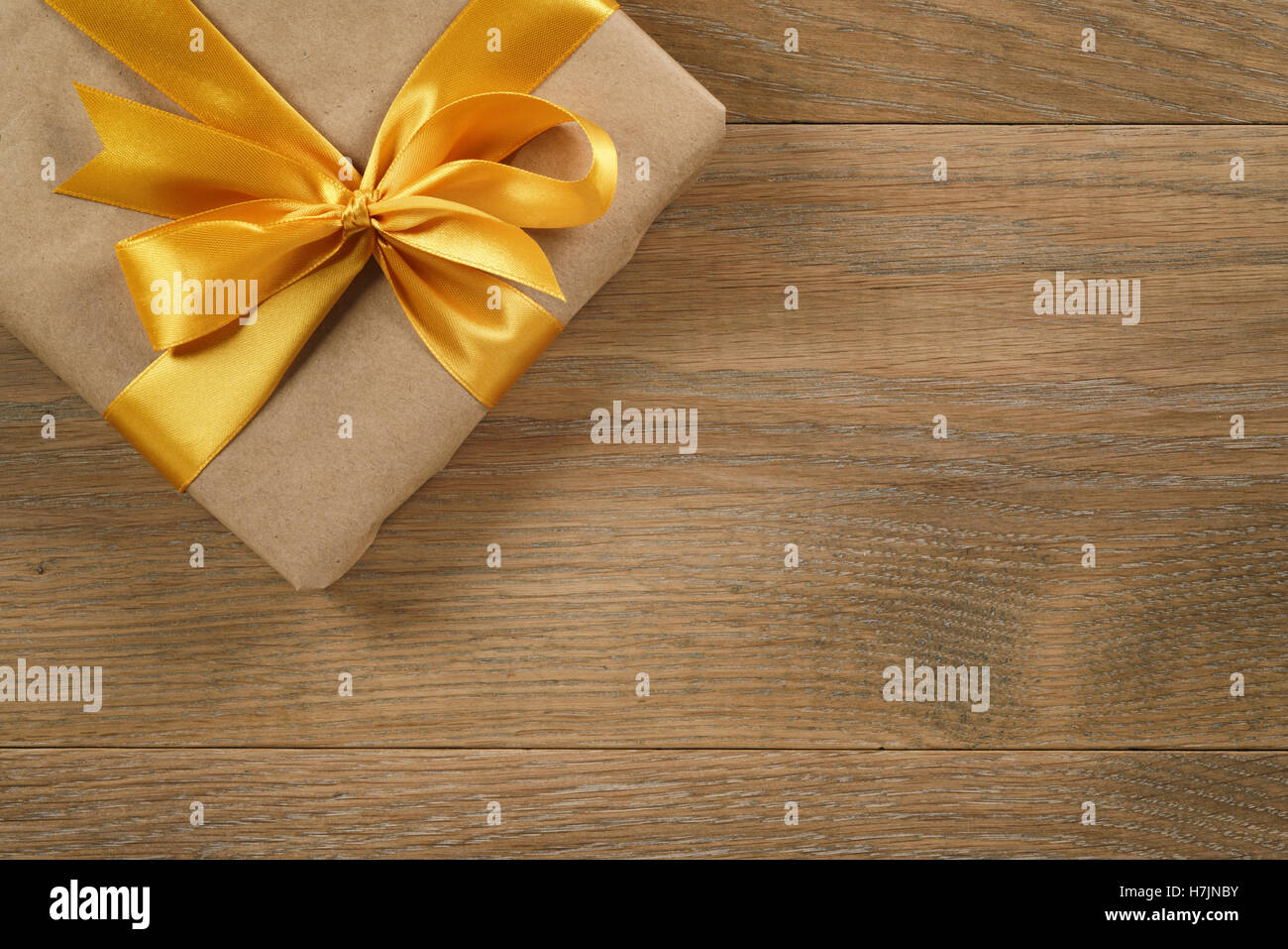 brown gift box with golden ribbon bow on wooden oak table from above Stock Photo